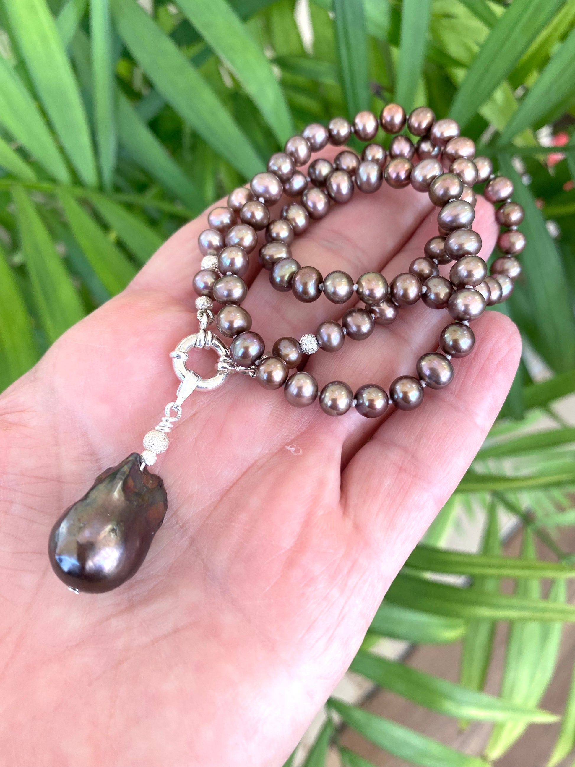 Bronze pearl necklace with brown baroque pendant held in hand, showing handcrafted detail and subtle color contrast.