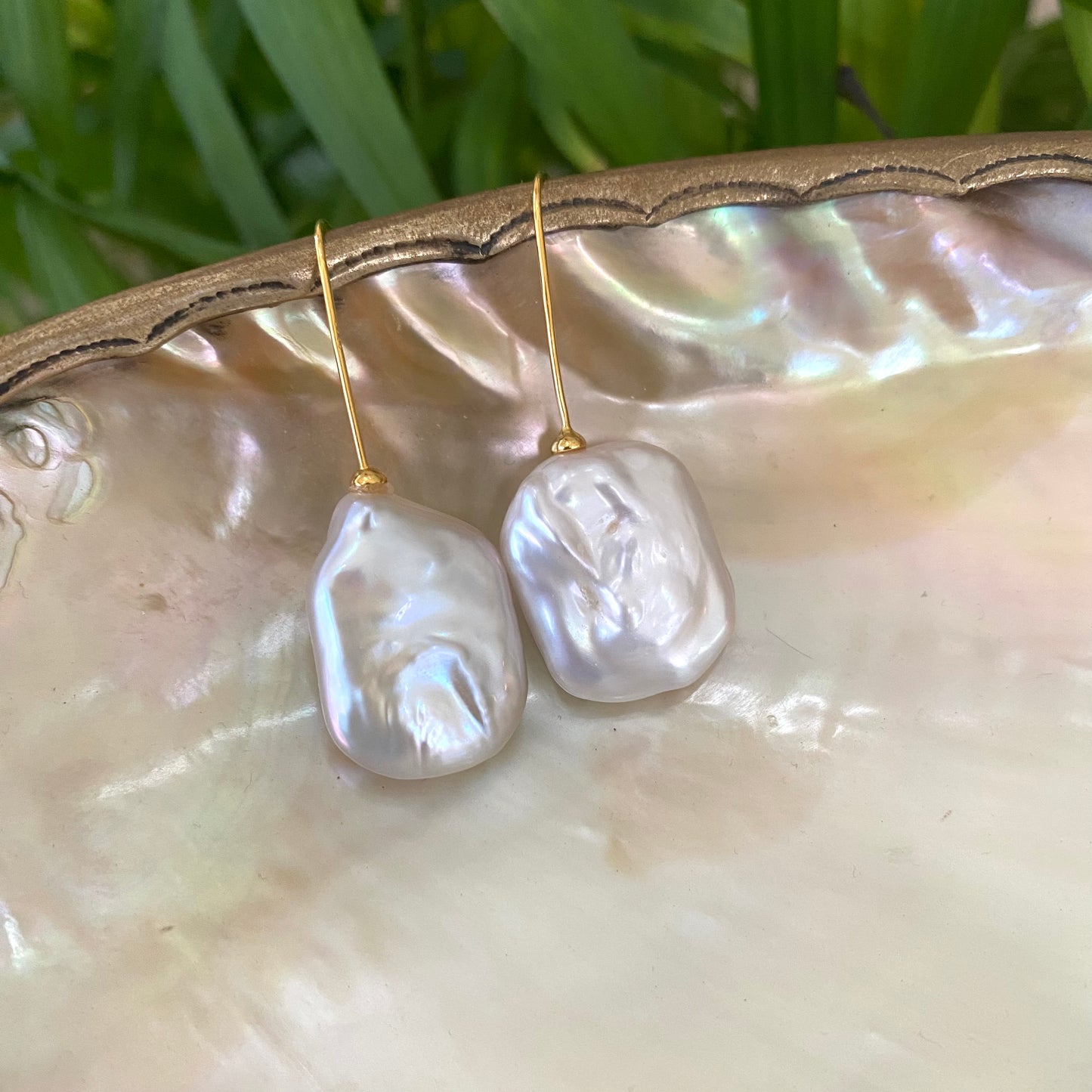White freshwater pearl drop earrings gold vermeil version resting on shell with green foliage, handcrafted in Canada.