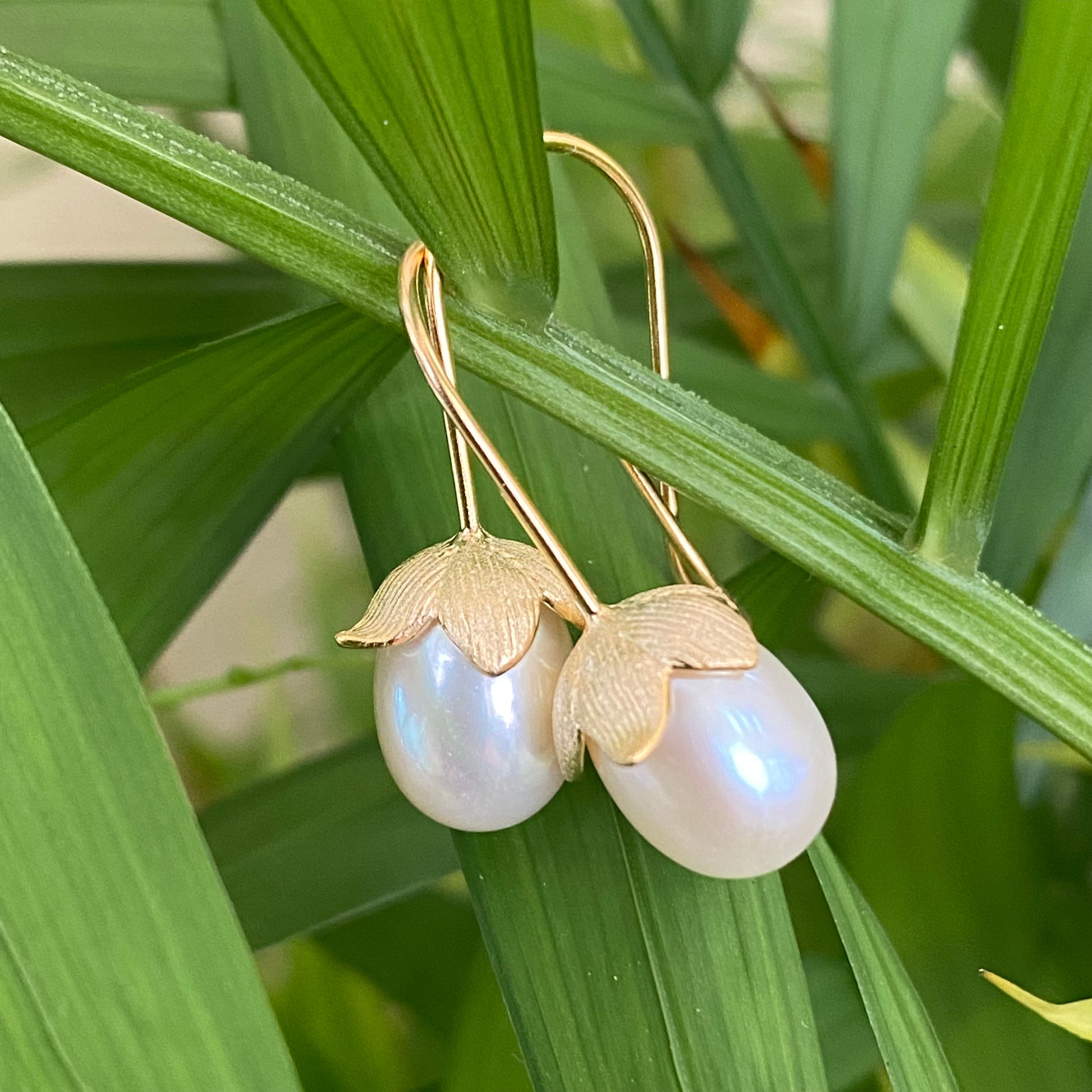 Rice Pearl Earrings – gold tulip hooks dangling from green leaves in close-up