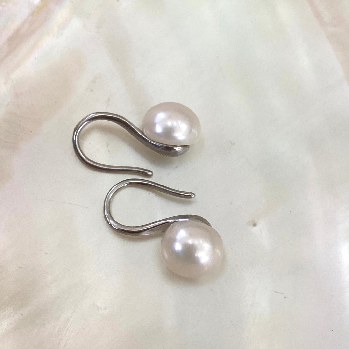 Button Pearl Earrings – silver version close-up against white pearl shell background