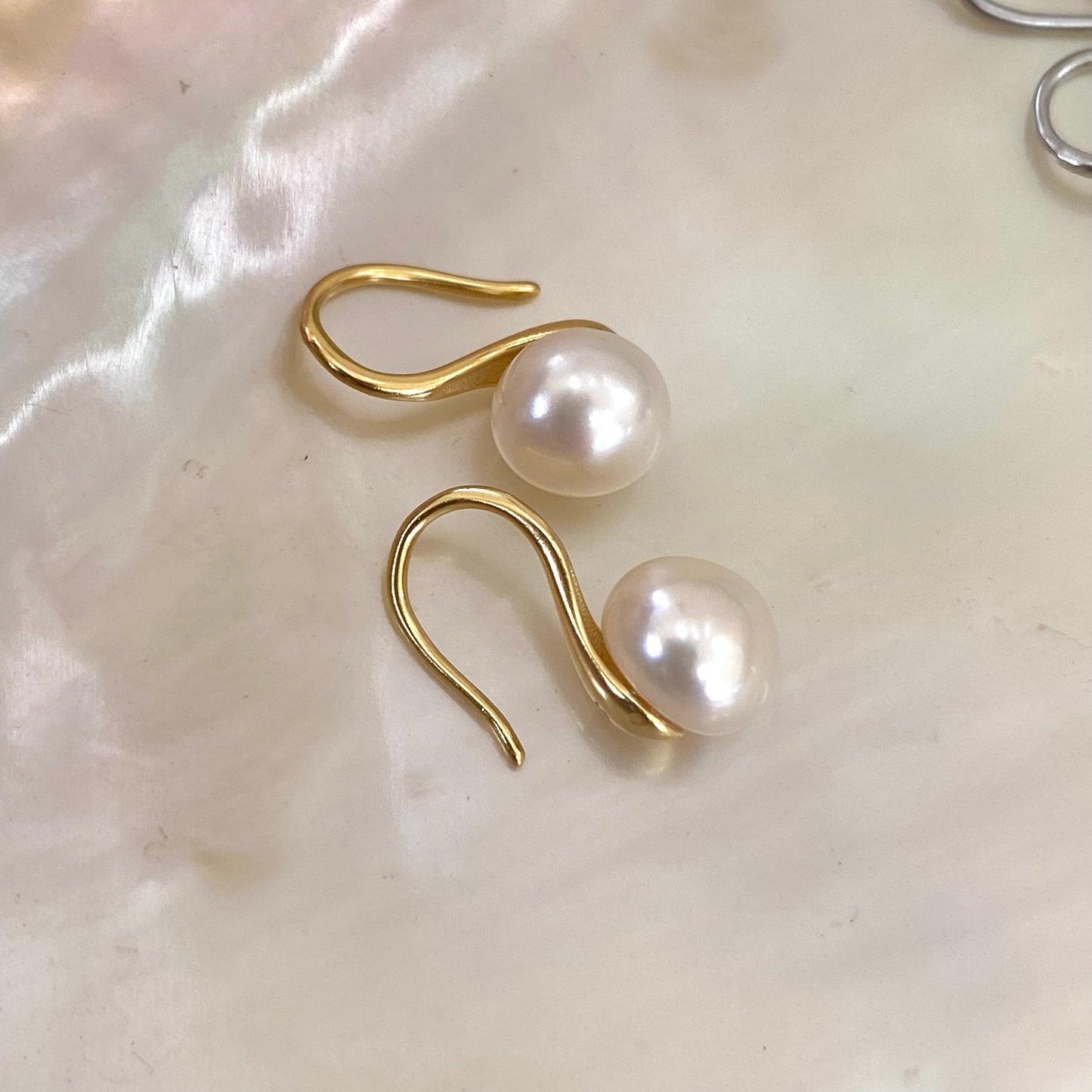 Button Pearl Earrings – gold version close-up displayed on white pearl shell