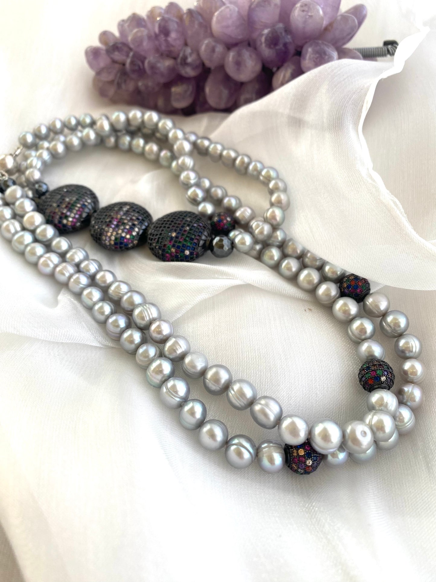 Double-strand Grey Pearl Necklace showcasing freshwater pearls and CZ embellishments beside amethyst on white cloth.
