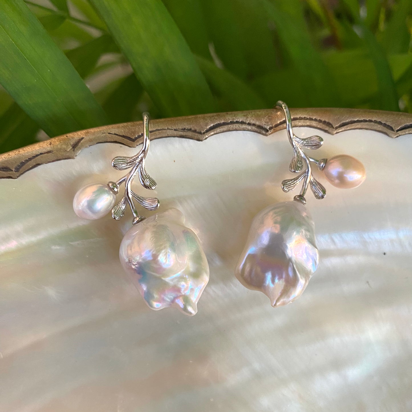 Baroque pearl earrings in silver displayed on pearl shell and green leaf backdrop
