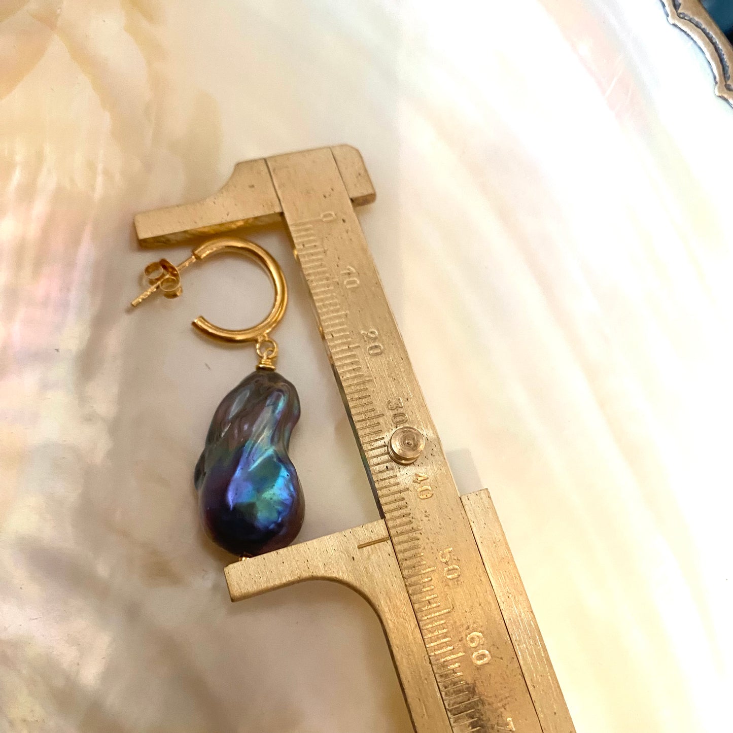 Baroque pearl hoop earrings measured by ruler for size on white background