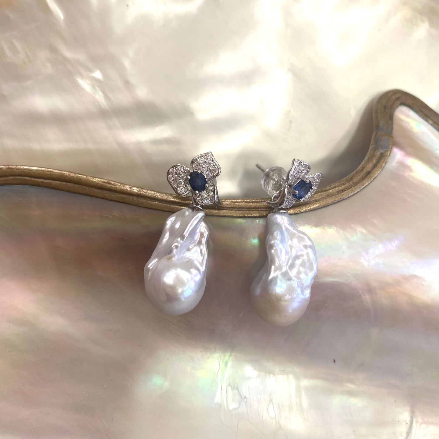 Close view of sapphire and emerald stud earrings with pearl drops on shell background