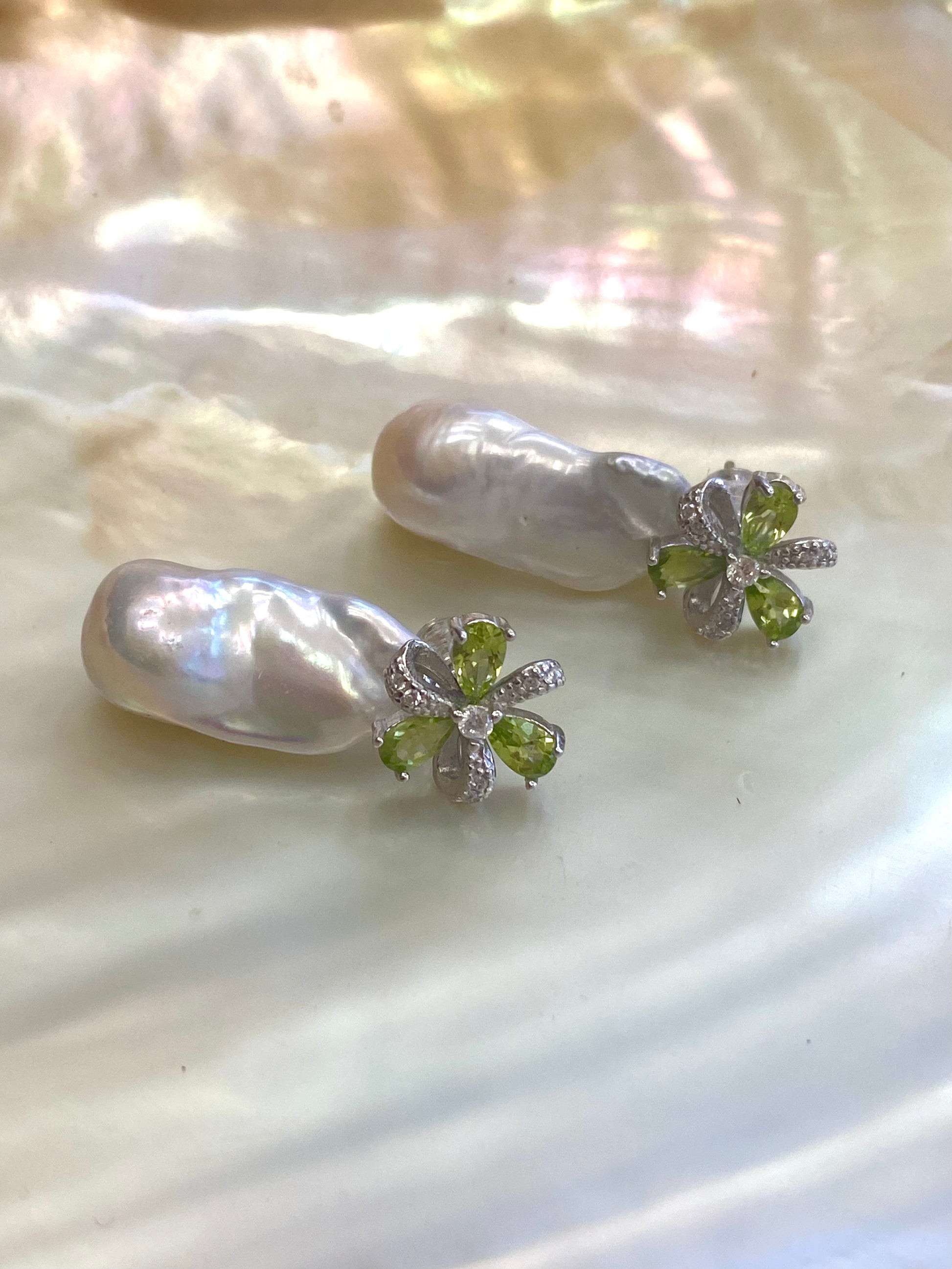 Close view of Peridot stud earrings with baroque pearl drops on pearl shell