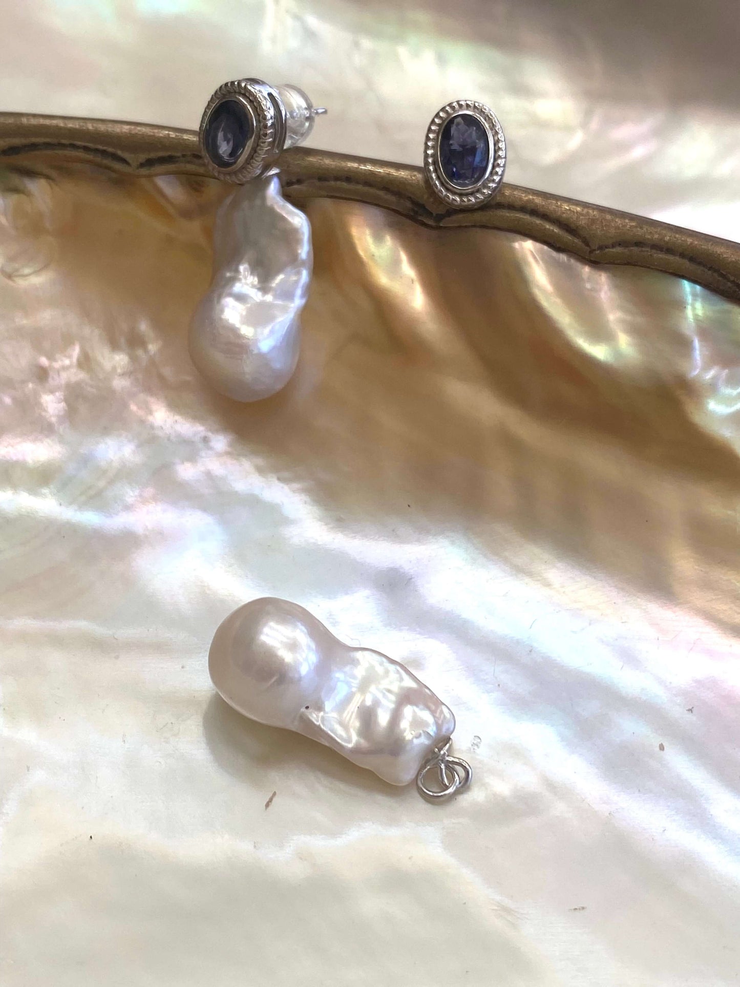 Close-up of iolite baroque pearl drop earrings on white pearl shell backdrop — sterling silver and gemstone design by Loulia Pearl Jewelry