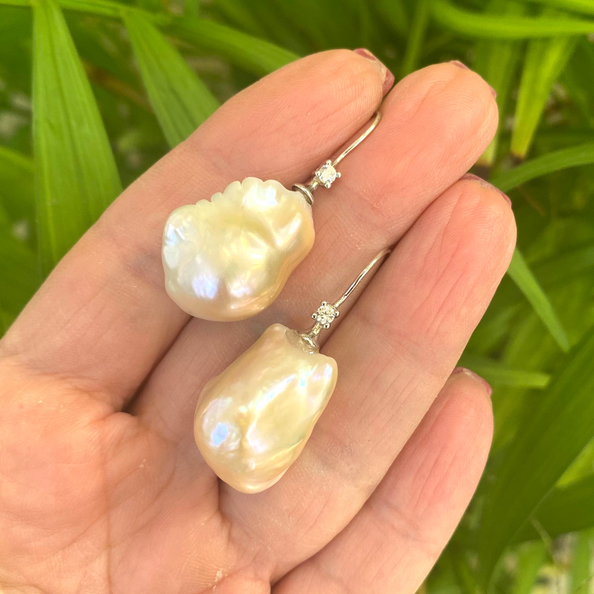 Golden Baroque Pearl Earrings – held by hand against green leaf backdrop