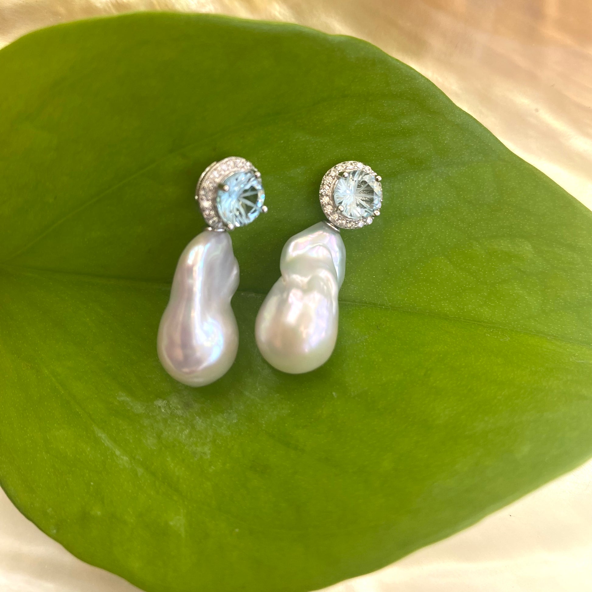 Blue topaz pearl drop earrings with removable baroque pearls against green leaf