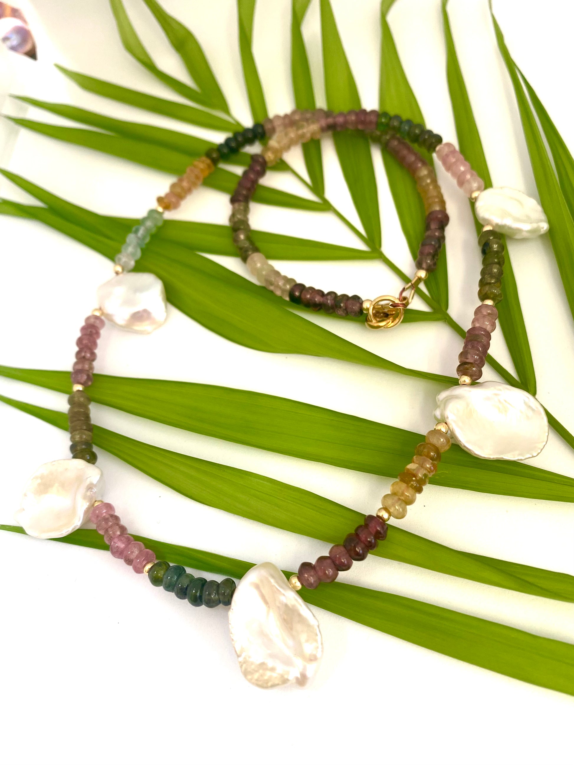 Multi tourmaline and keshi pearl necklace displayed on white and green leaf backdrop, boho-chic style.