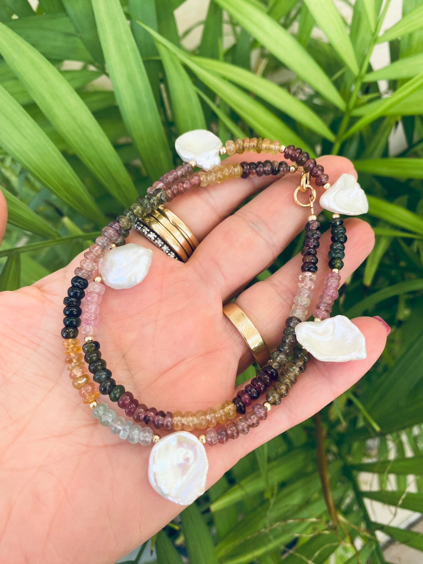 Multi tourmaline and keshi pearl necklace held in hand against green leaves, natural gemstone jewelry.