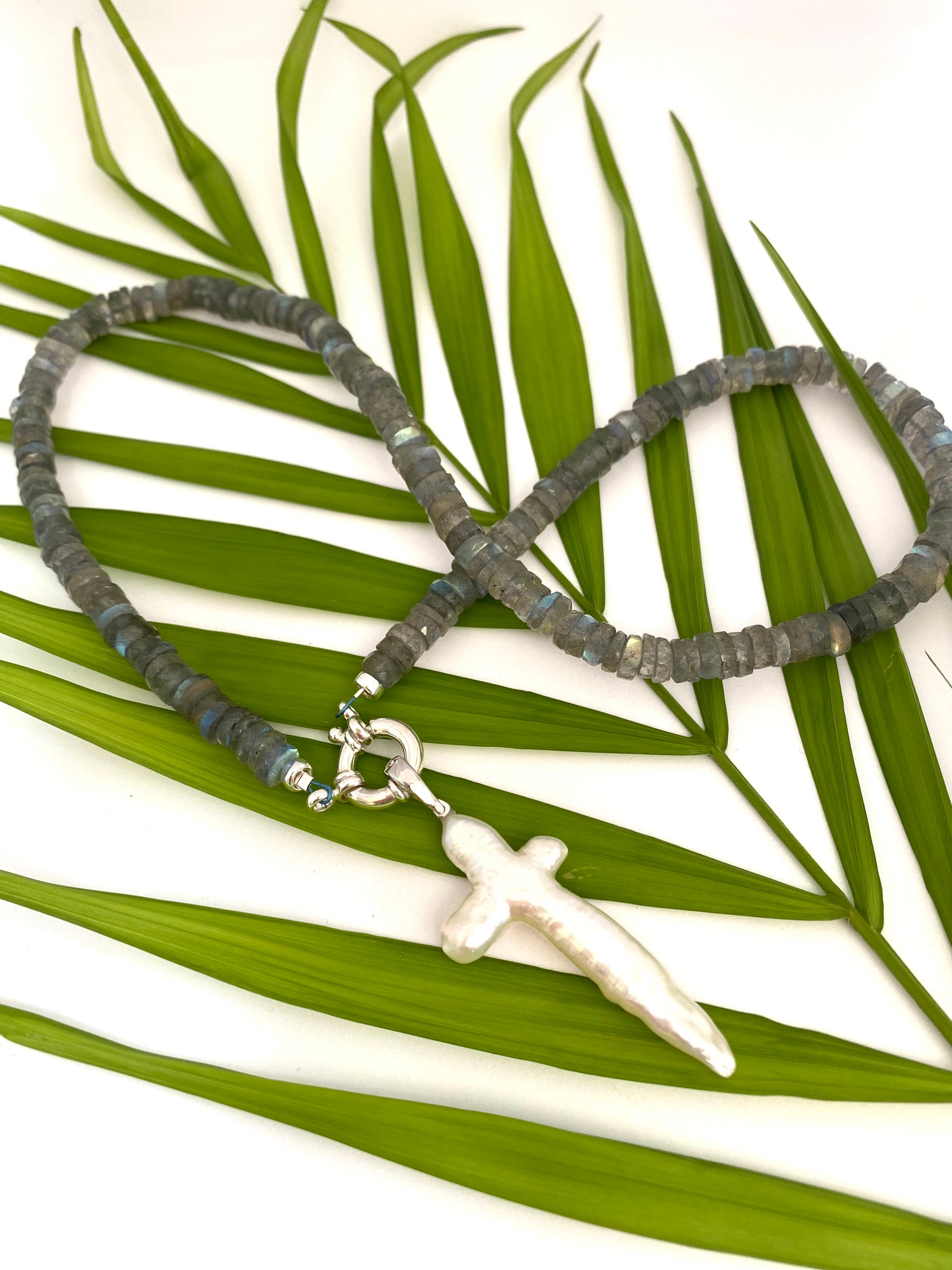 Handcrafted labradorite necklace with pearl cross photographed outdoors with green leaves — artisan jewelry by Loulia Pearl Jewelry