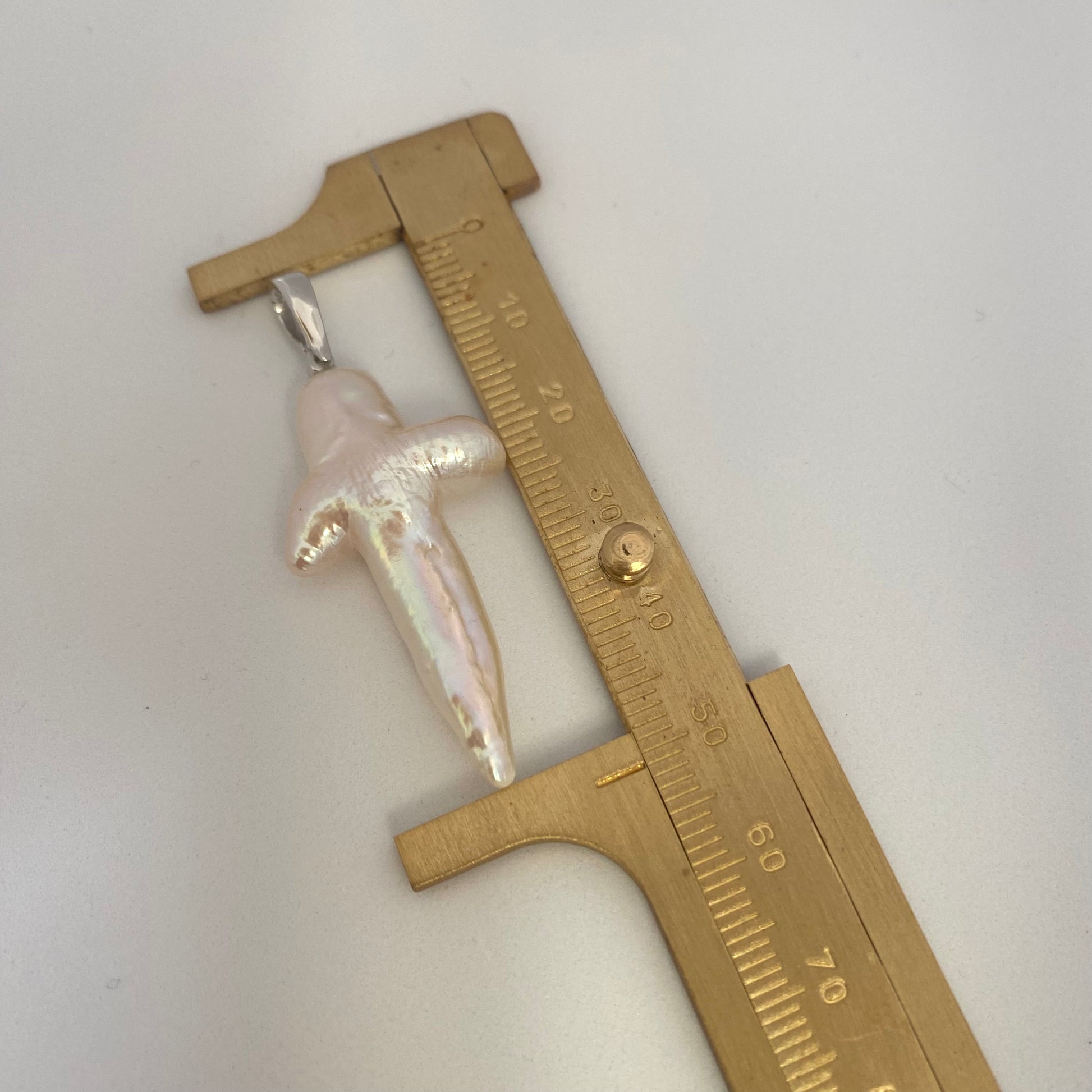 Baroque pearl cross pendant close-up beside ruler showing size and natural luster.