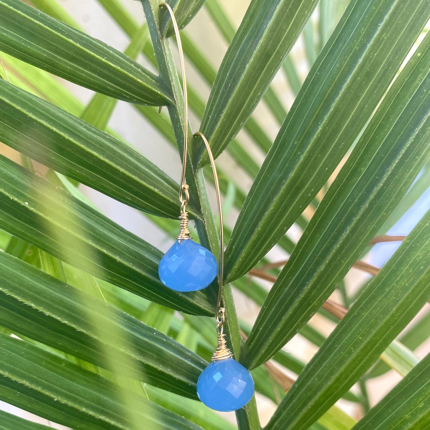 Chalcedony threader earrings featuring blue briolettes hanging gracefully against green palm leaves.