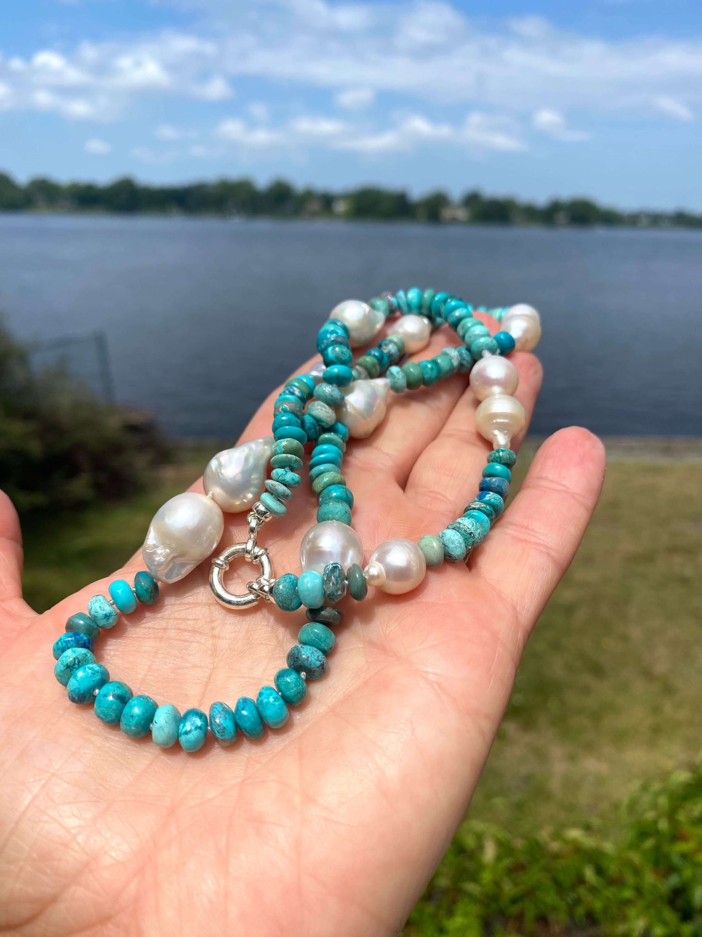 Arizona turquoise pearl necklace shown in hand beside a lake, featuring turquoise rondelle beads and large pearls.