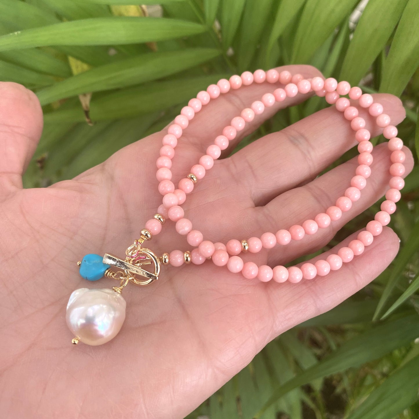Pink coral toggle necklace with baroque pearl and turquoise charm, showcasing handcrafted beads in vibrant colors.
