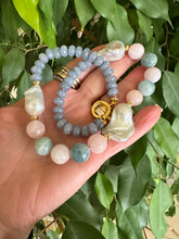 Cargar imagen en el visor de la galería, Blue jade morganite aquamarine pearl necklace showcasing baroque gem design, held in hand among lush foliage.
