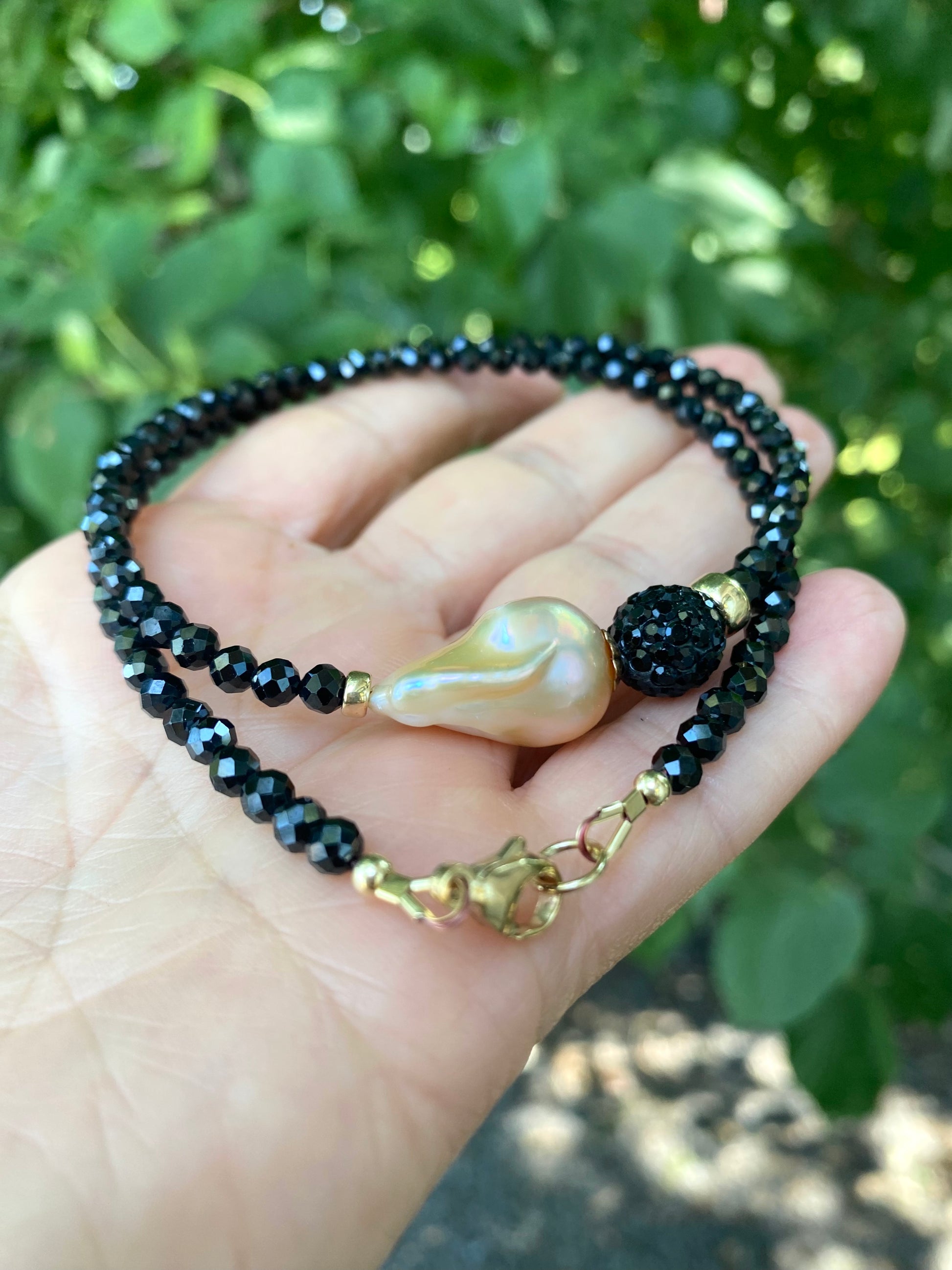 Black spinel pearl necklace held in hand against green foliage