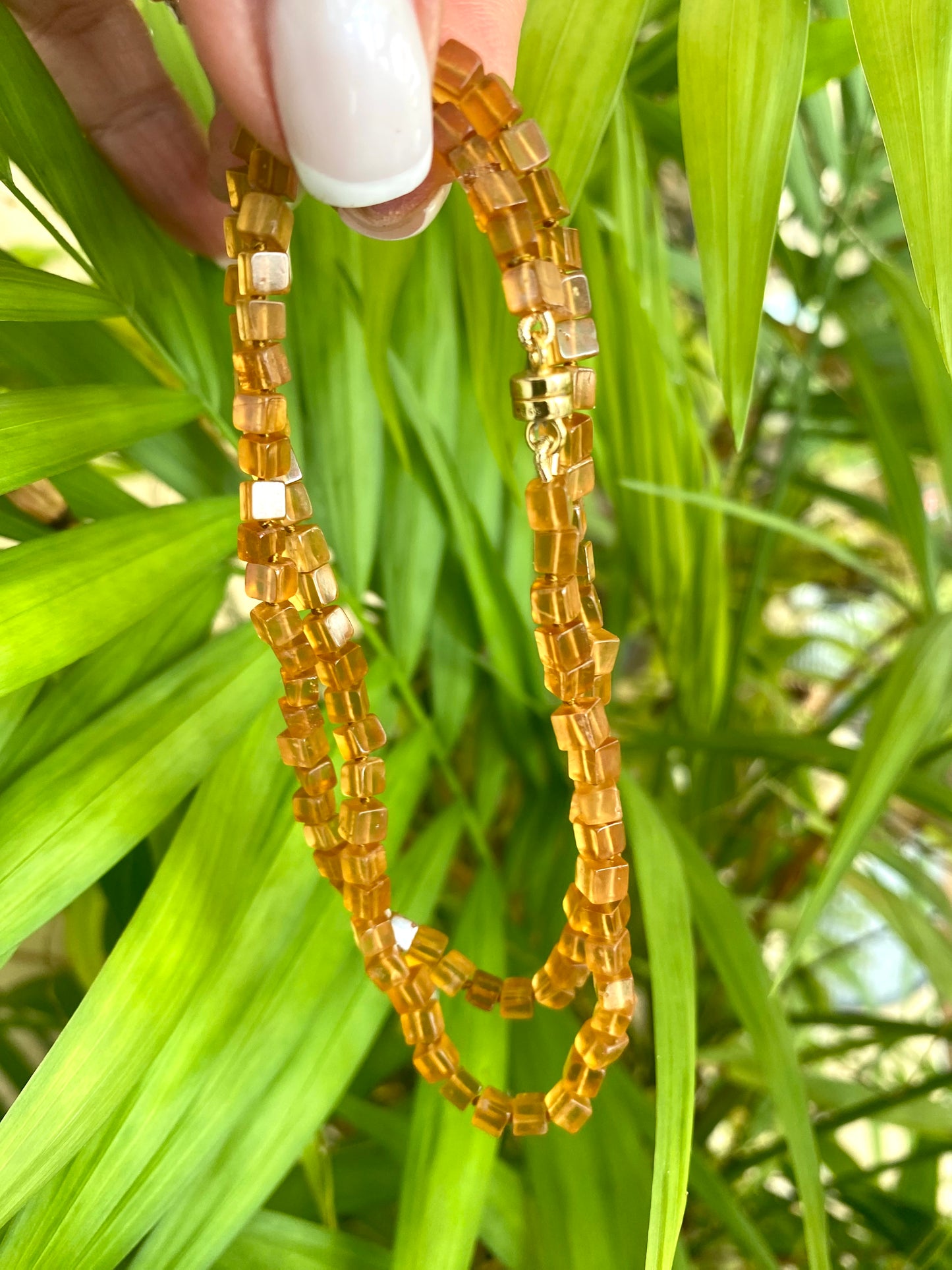 Hessonite garnet necklace with magnetic clasp showcasing rich golden-yellow tones against green foliage.
