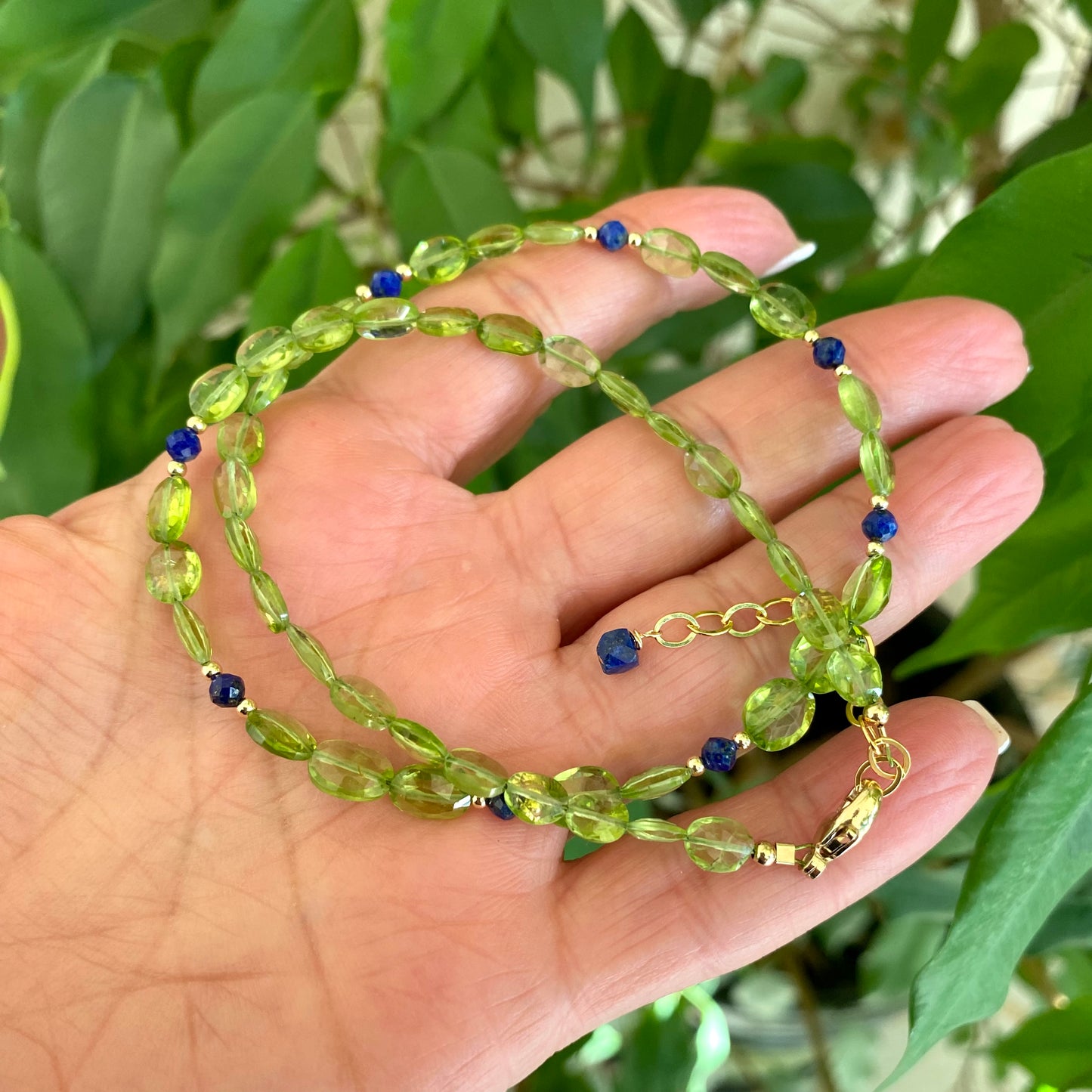 Peridot lapis necklace featuring vibrant green peridot oval beads and blue lapis lazuli accents, held in hand.