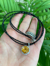 Lade das Bild in den Galerie-Viewer, Hand holding black spinel and citrine pendant necklace near green leaf background
