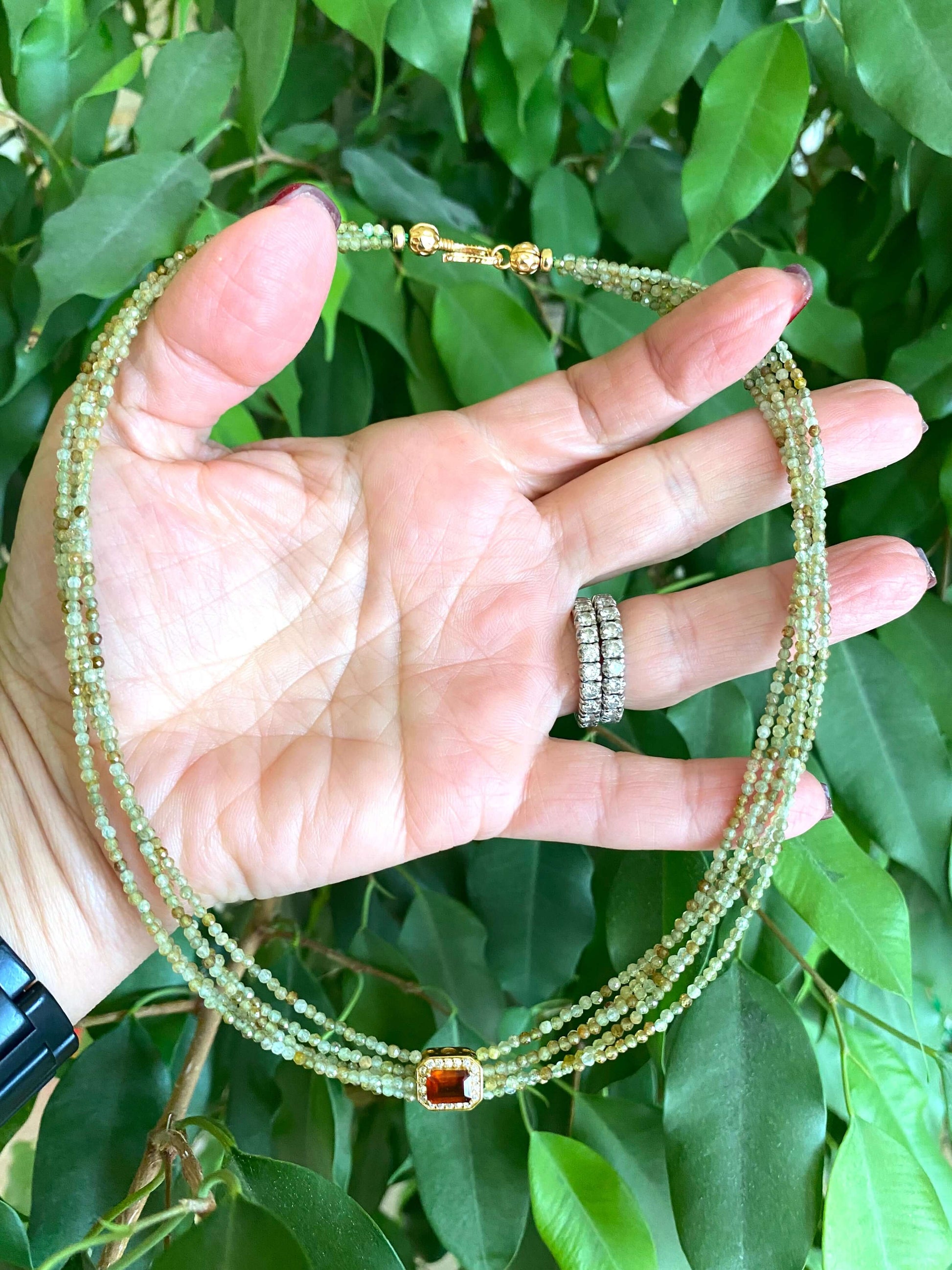Green orange garnet necklace displayed in hand, showcasing multi-strand gold vermeil design and color details.
