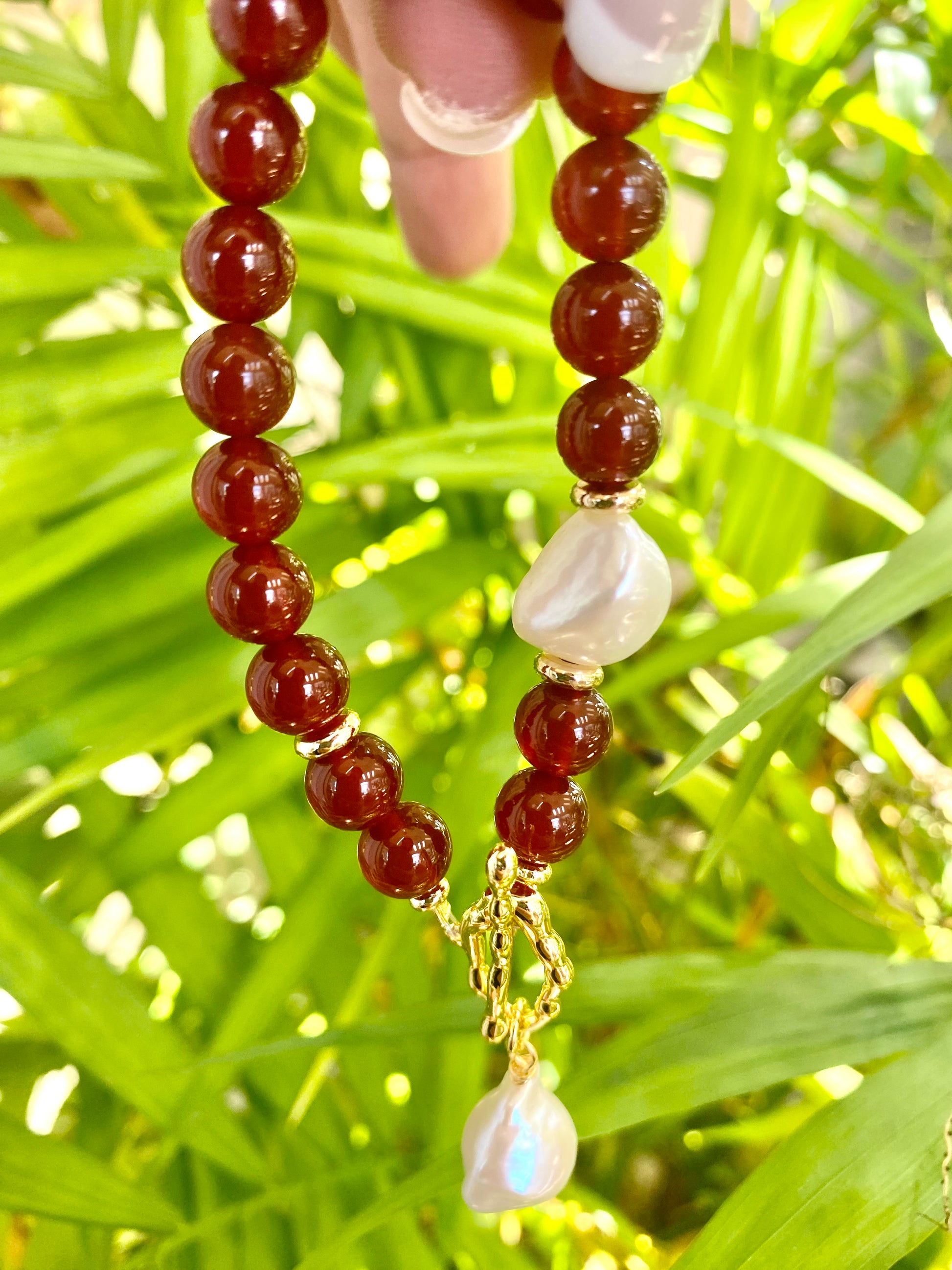 carnelian pearl bracelet featuring burnt orange carnelian beads and a white baroque pearl, showcased in a vibrant green setting.