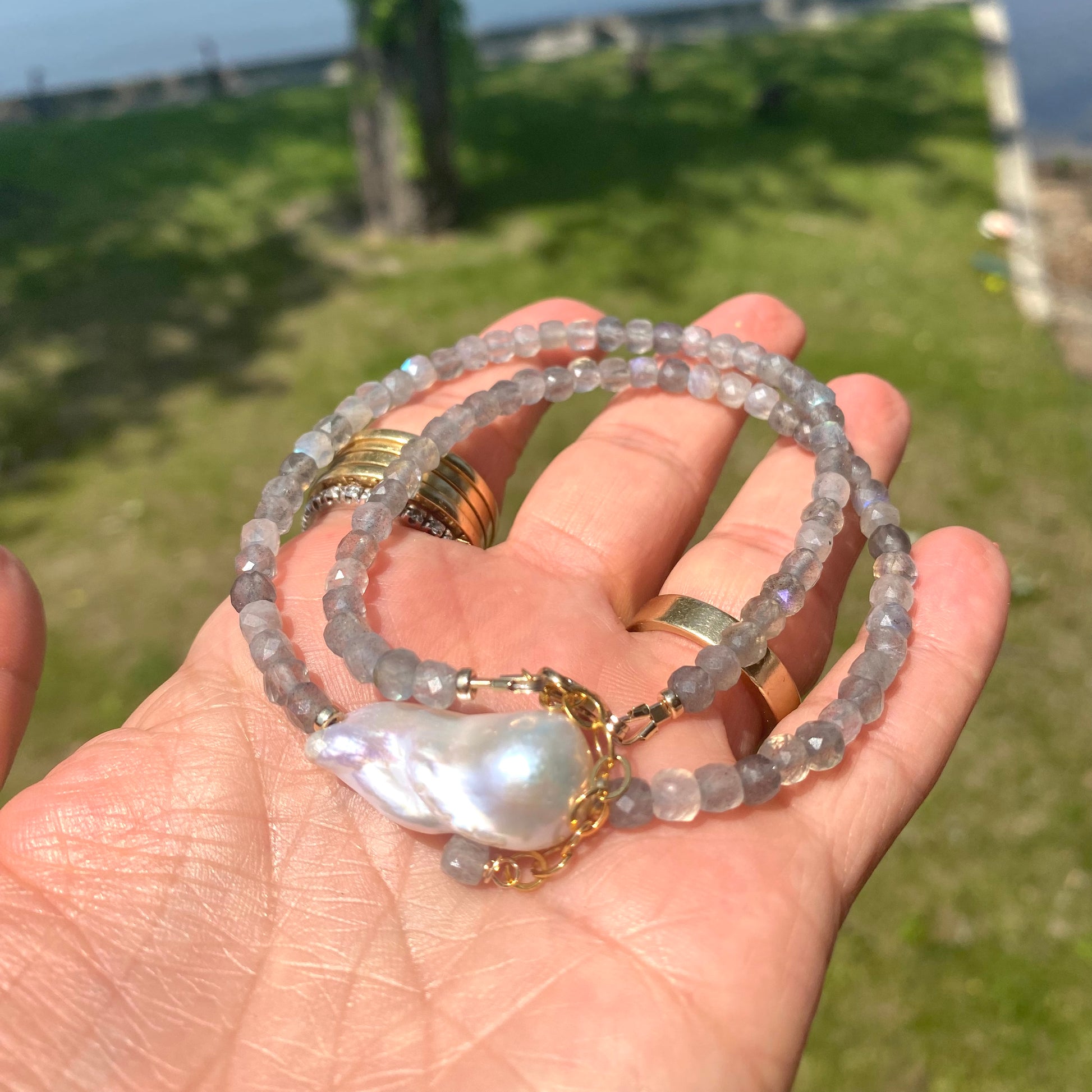 labradorite necklace with blue flash and baroque pearl displayed in hand against a natural background.