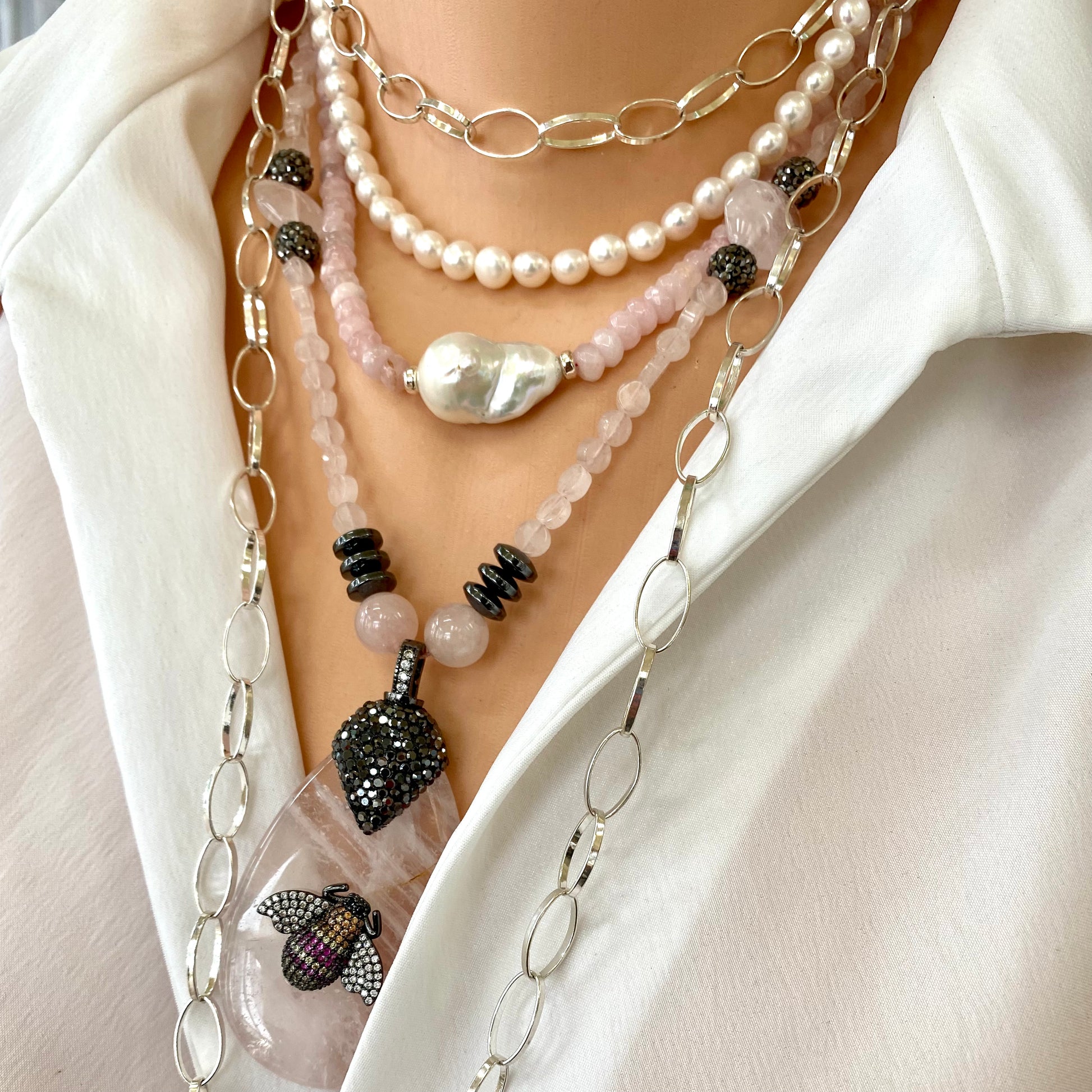 Rose quartz necklace with rhinestone pavé bee pendant and multi-layered strands with pearl and gemstone details.