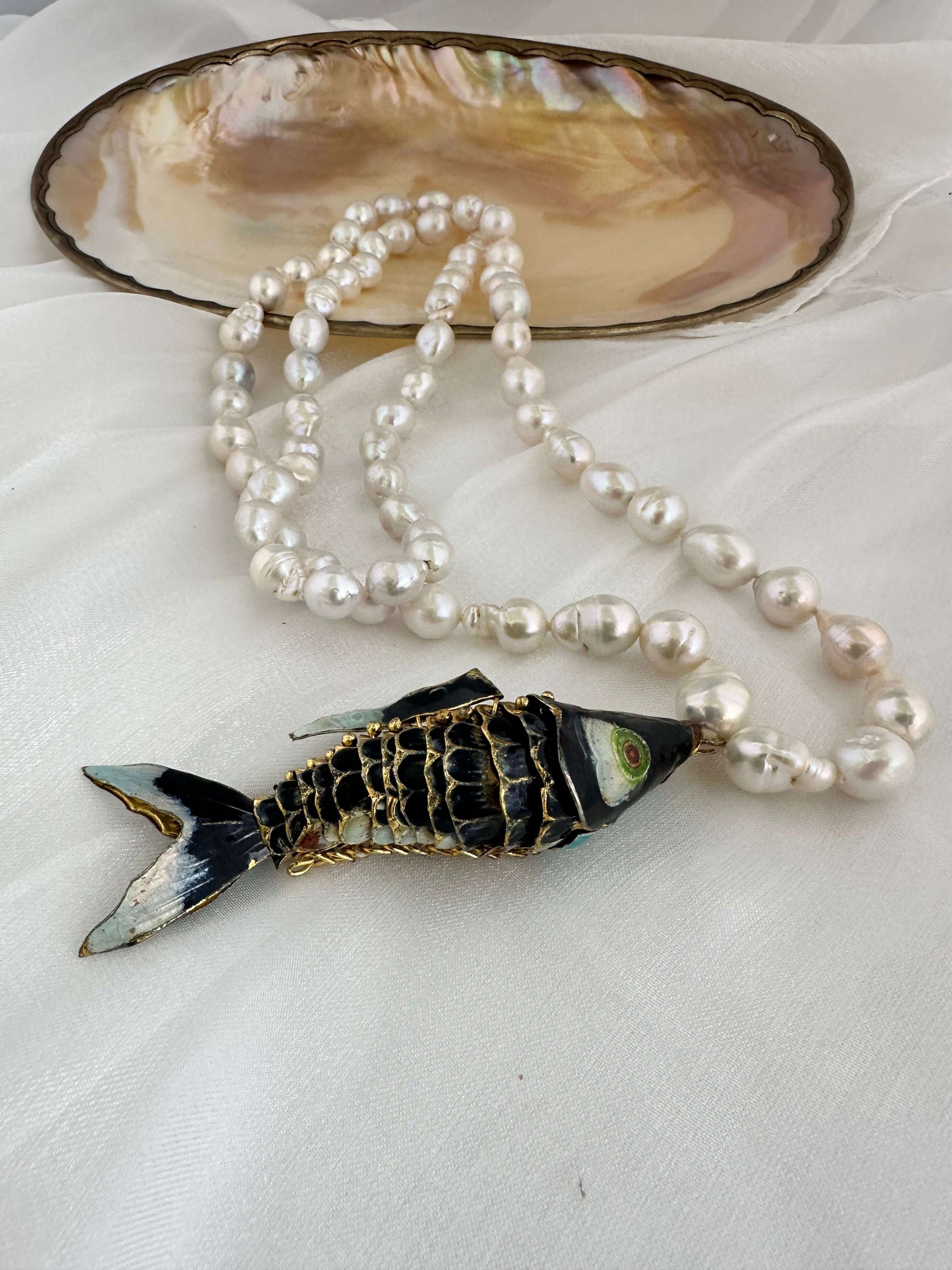 Fish pendant pearl necklace featuring a black cloisonné fish and white baroque pearls in a stylish arrangement.