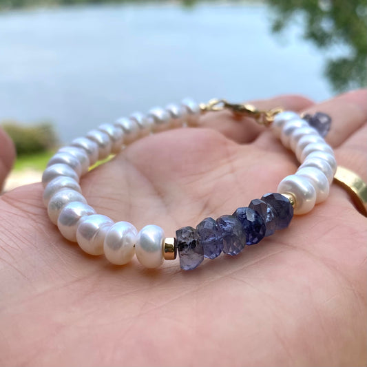 Iolite pearl bracelet featuring blue iolite rondelle beads and luminous white pearls held in a hand by a lake.