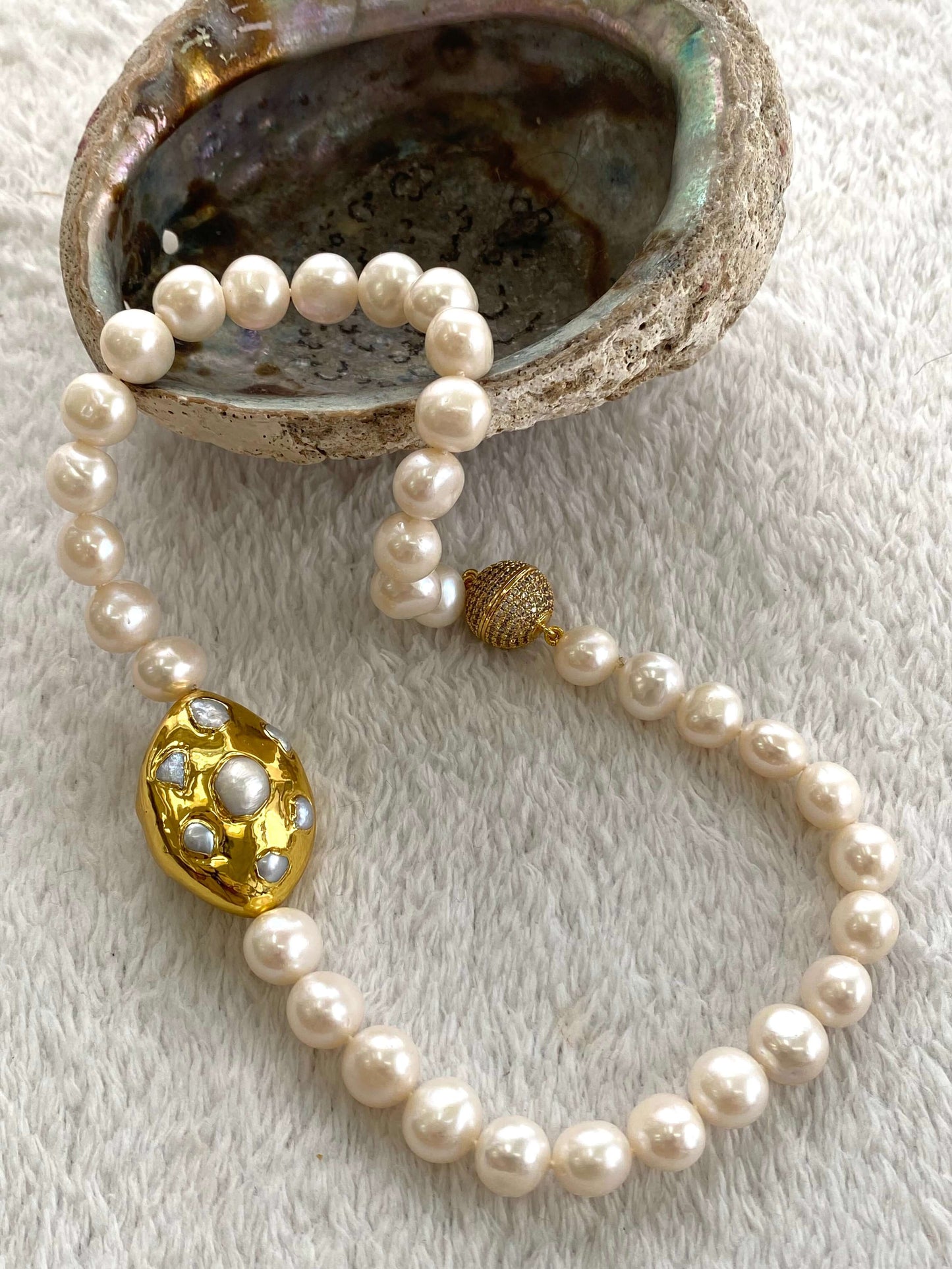 White potato pearl necklace with gold focal accent displayed on a textured surface.