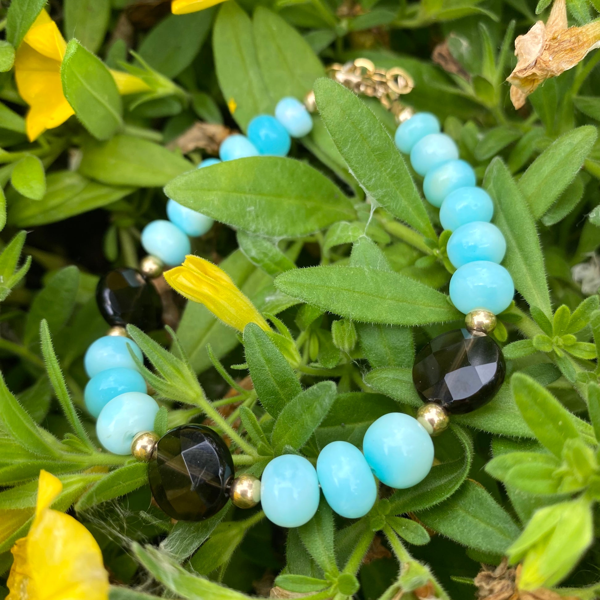 Opal quartz bracelet featuring sky blue opal and smoky quartz set against a backdrop of vibrant green foliage.