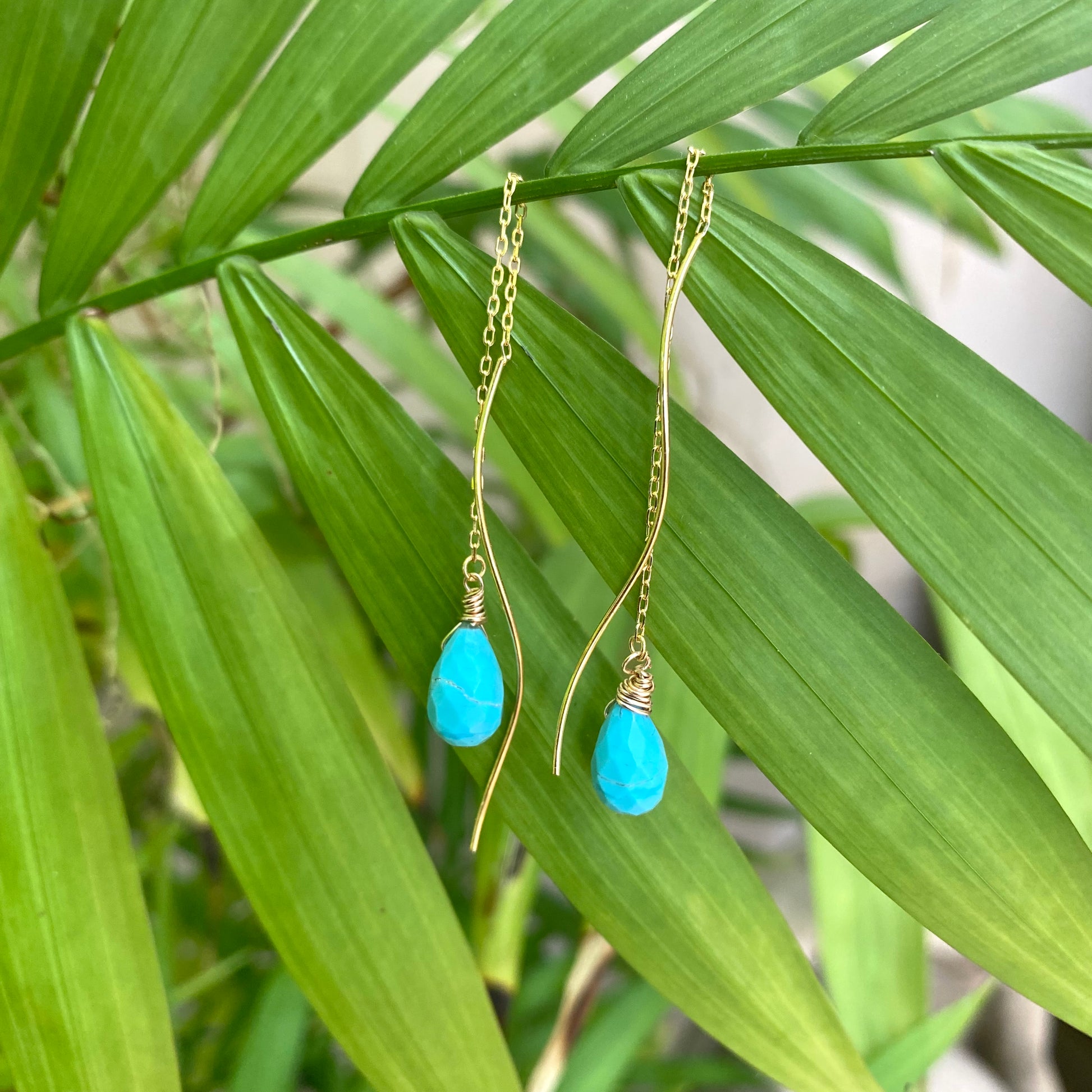 Turquoise threader earrings featuring Arizona briolettes displayed against green foliage.