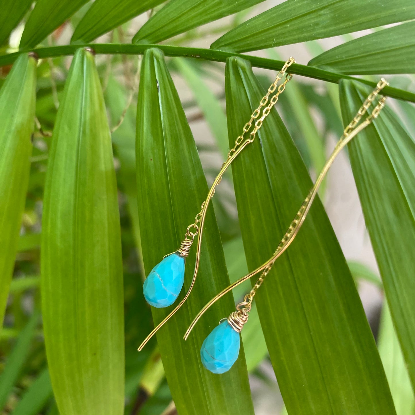 Turquoise threader earrings featuring Arizona briolettes on a backdrop of lush green leaves.