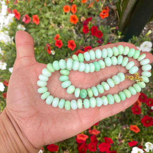 Green opal candy necklace displayed in a hand amidst colorful flowers.