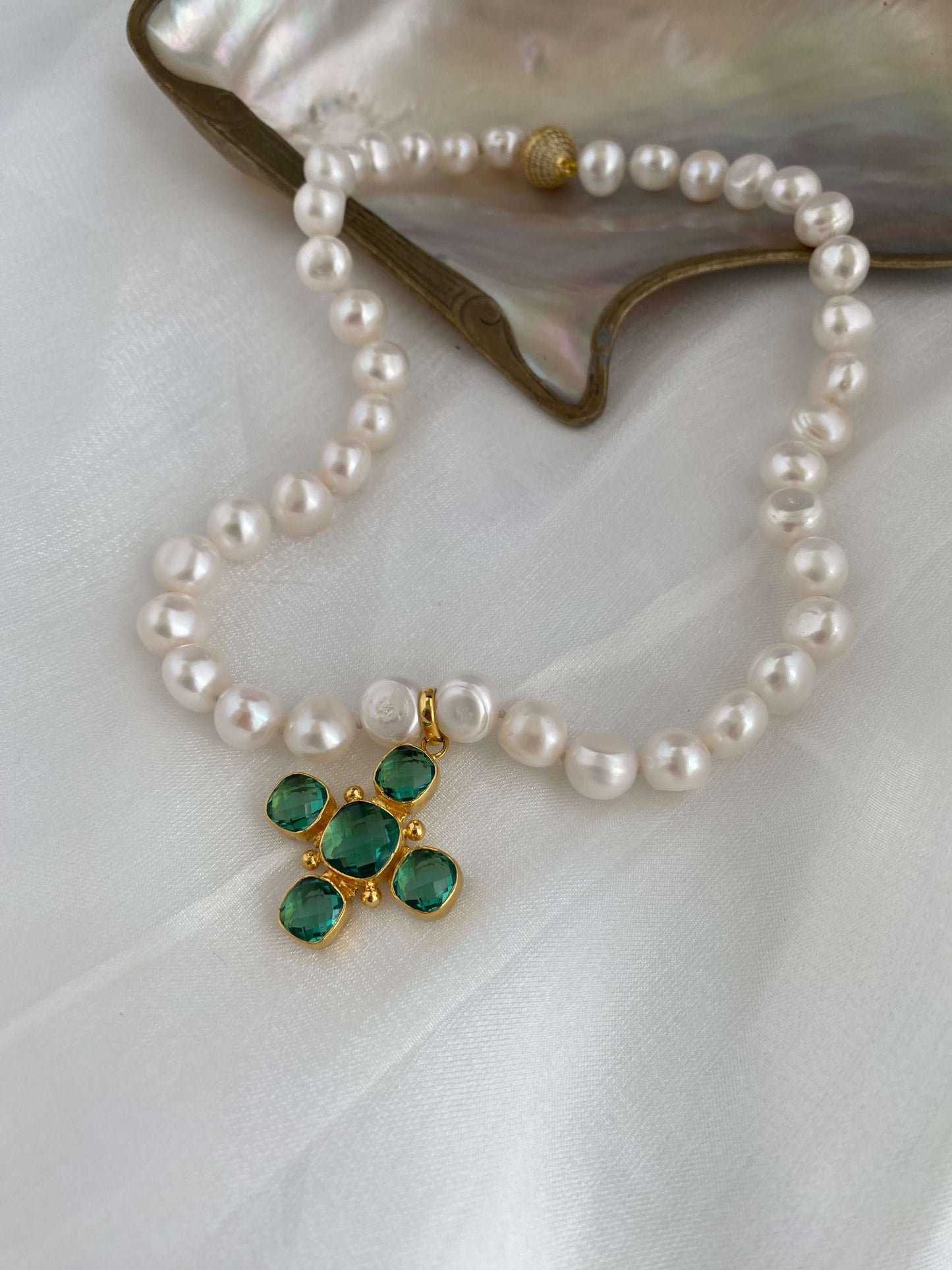 Potato pearl necklace with cross pendant featuring green quartz centerpiece on silk background.