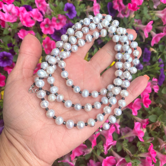 Light grey freshwater pearl necklace displayed in hand against colorful flower background.