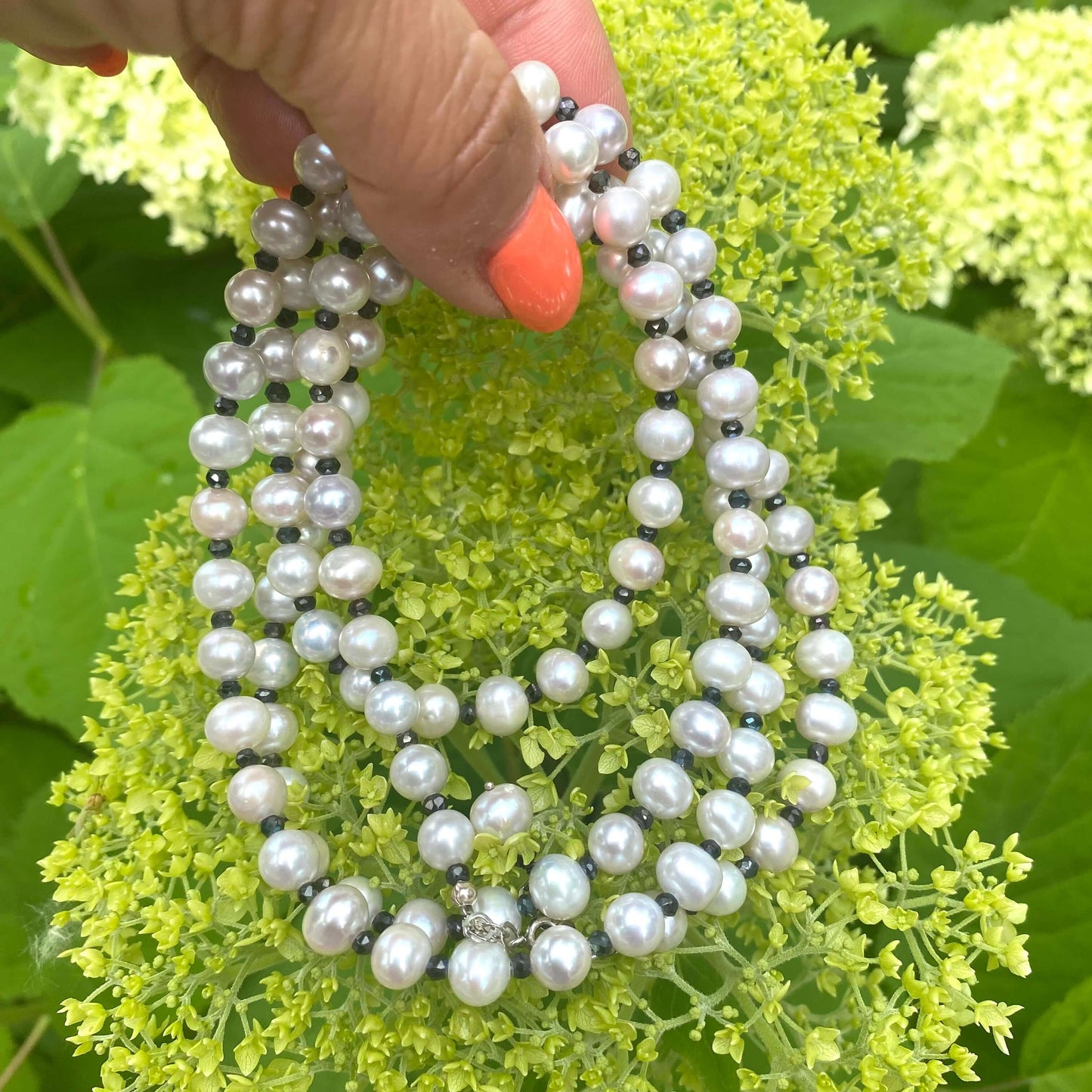 Light grey freshwater pearl necklace displayed in hand with greenery in the background.
