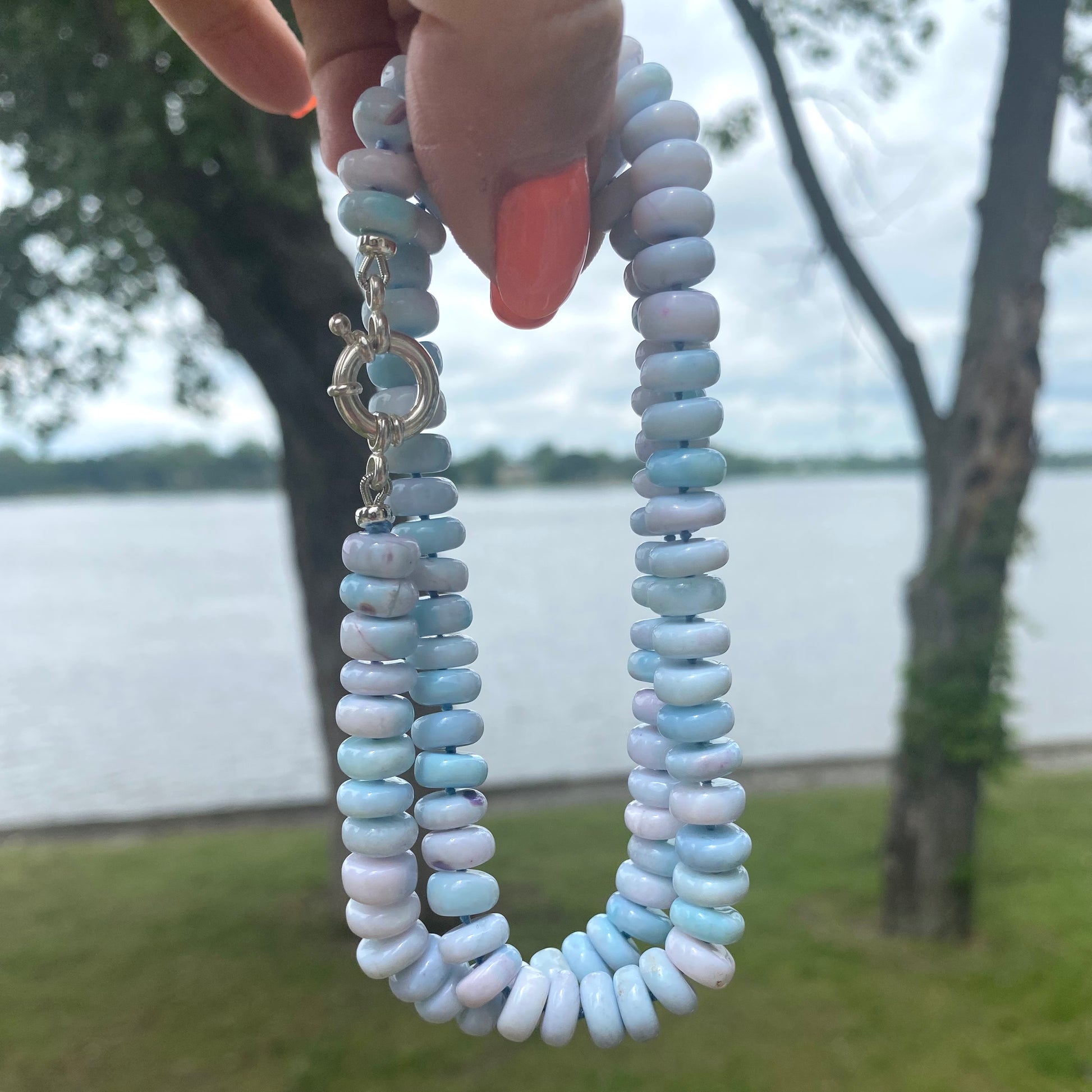 Opal candy necklace in pinkish blue tones featuring smooth opal rondelle beads, displayed outdoors by a waterfront.