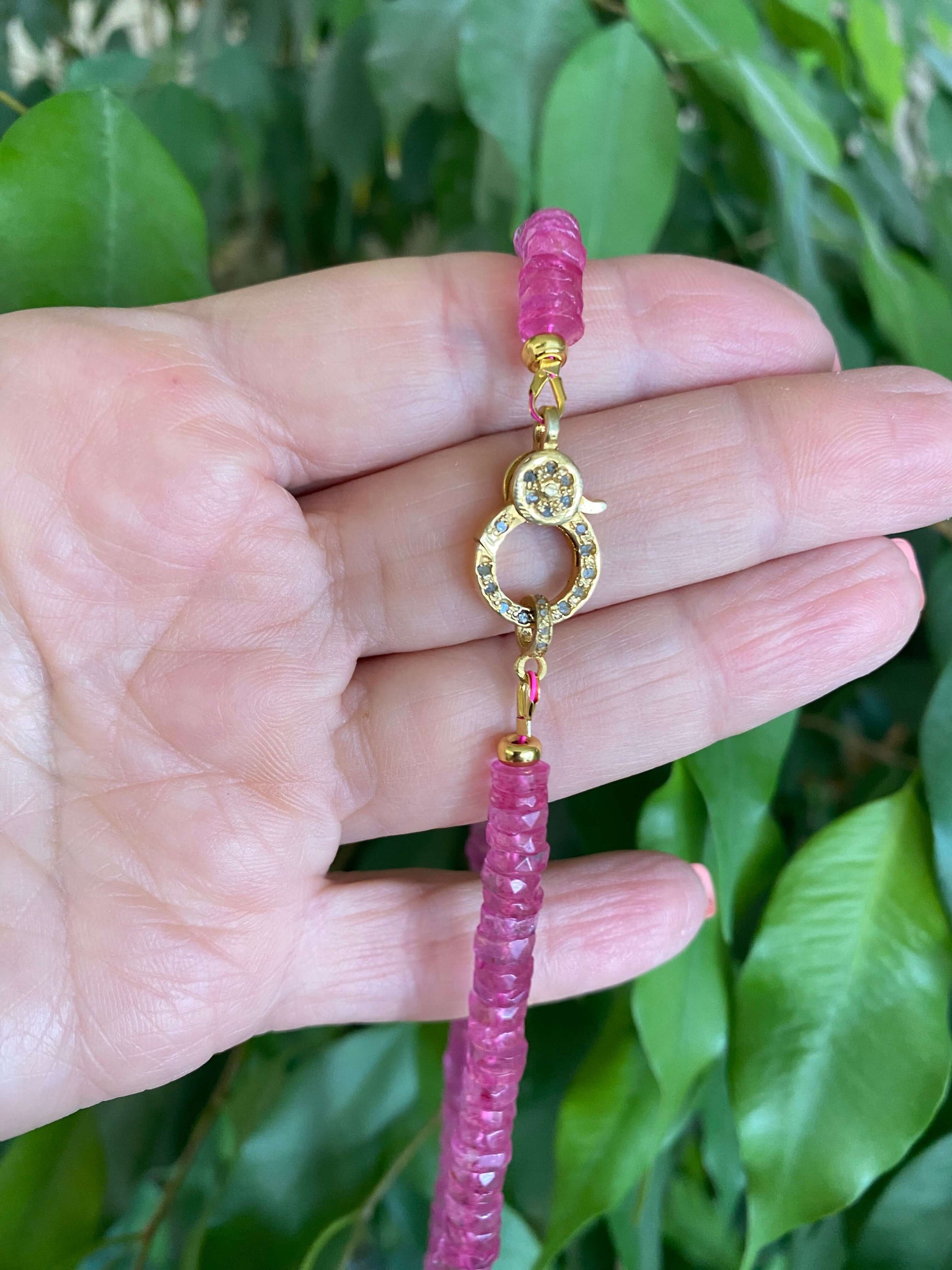 Close-up of a pink topaz beaded necklace with gold vermeil pavé clasp held in hand, showcasing the vibrant beads.