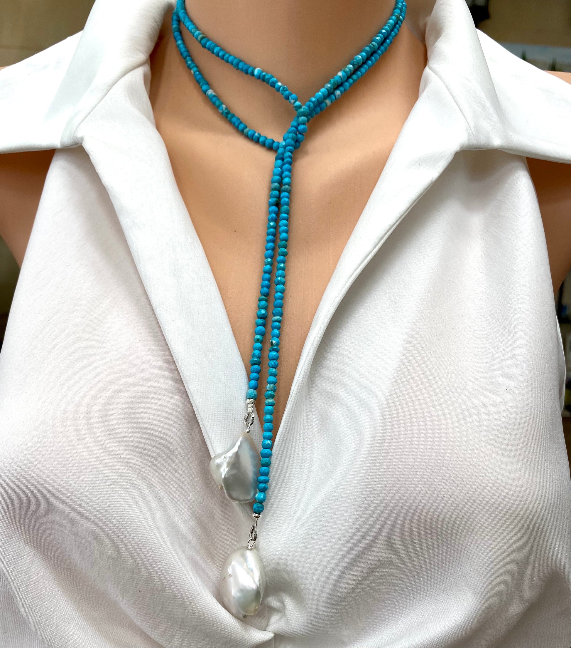 Turquoise lariat necklace with two baroque pearls showcased on a mannequin wearing a white shirt.