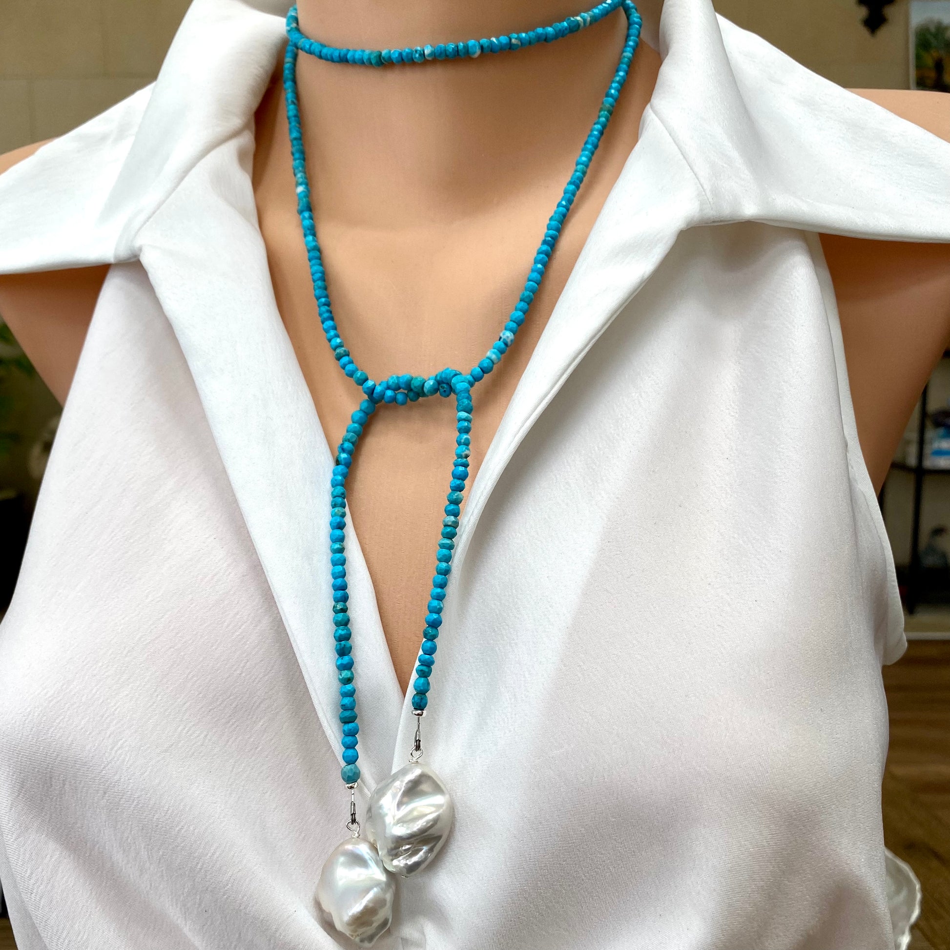 Turquoise lariat necklace with two baroque pearls elegantly displayed on a mannequin wearing a white shirt.