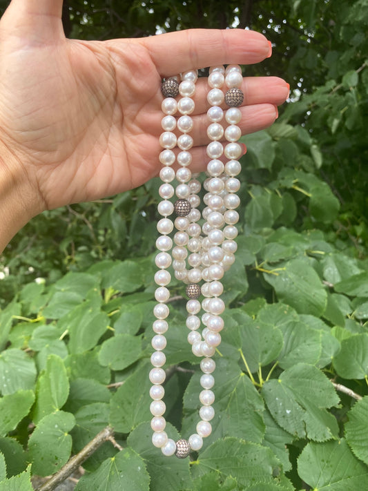 Handcrafted freshwater pearl necklace held against green leaf backdrop, handmade in Canada.