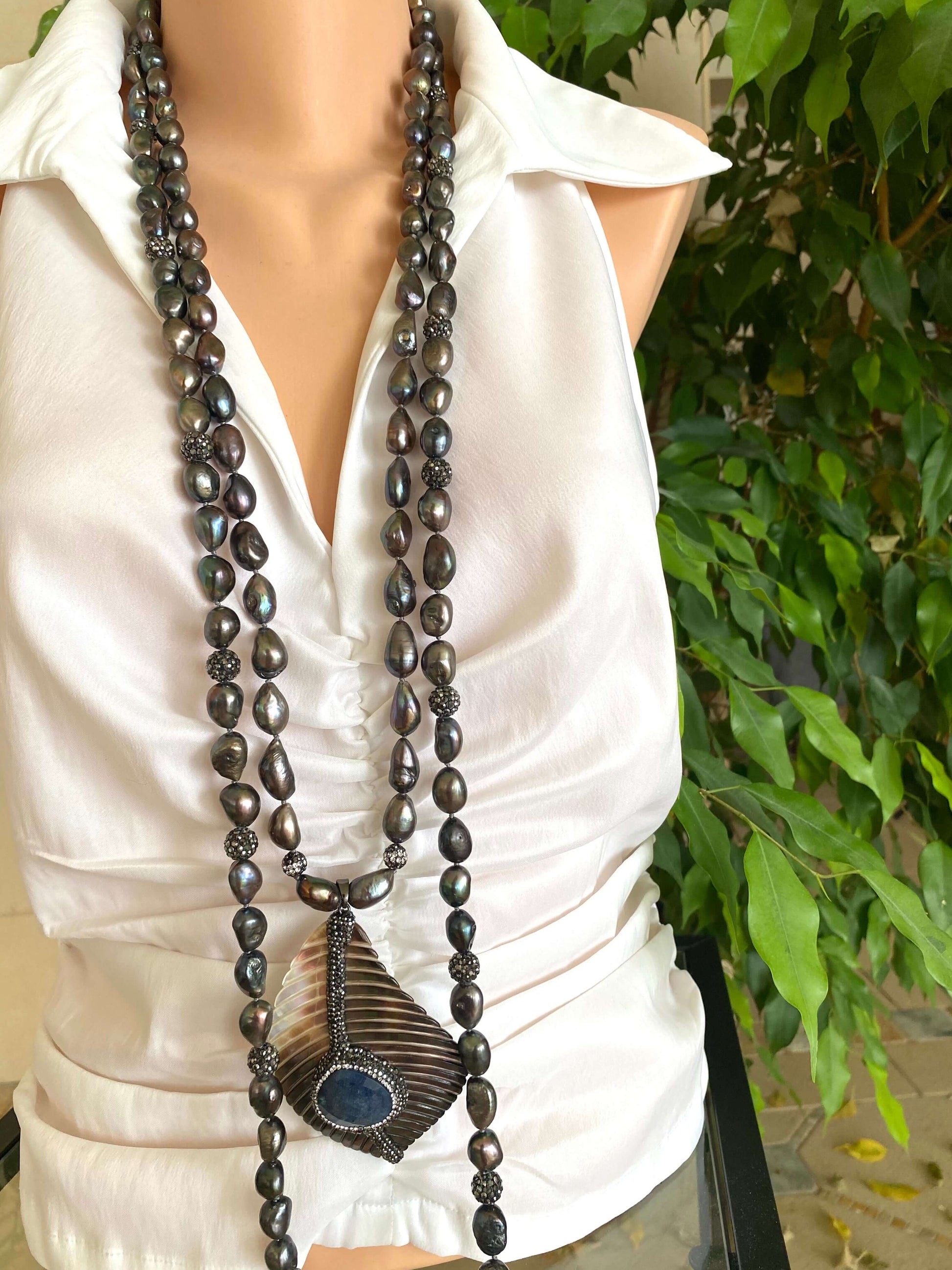 Long beaded necklace with a large pendant on a white shirt against a green leafy background