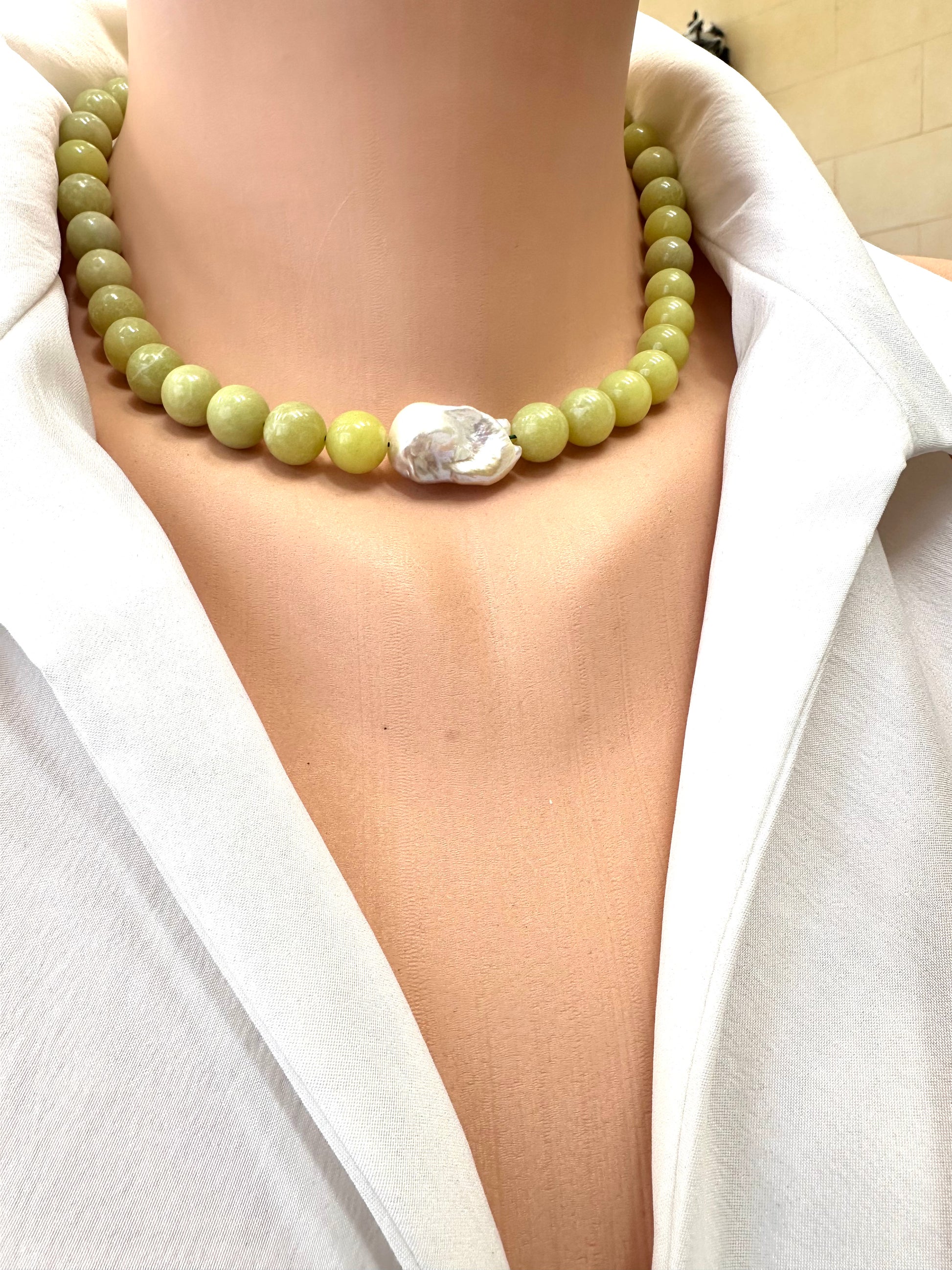 Necklace with green beads and a large white stone worn by a person in a white outfit.