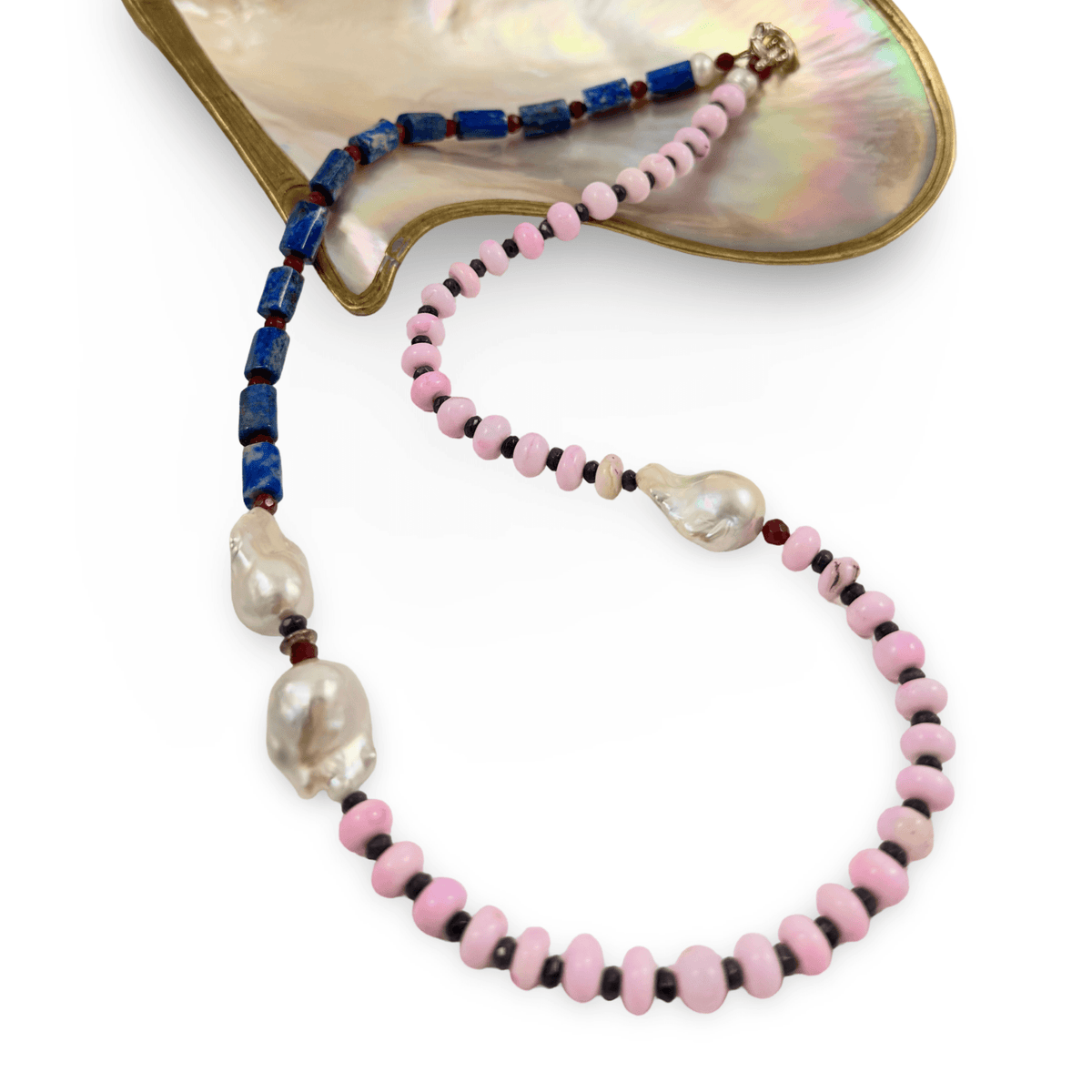 A beaded necklace with light pink round beads, dark blue rectangular beads, and large irregular white baroque pearls, displayed on a mother-of-pearl shell-shaped prop against a white background.
