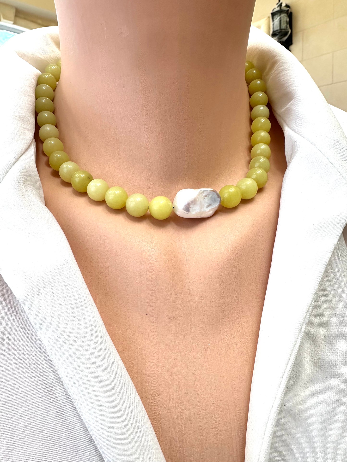 Necklace with green beads and a large white stone worn by a person in a white outfit.