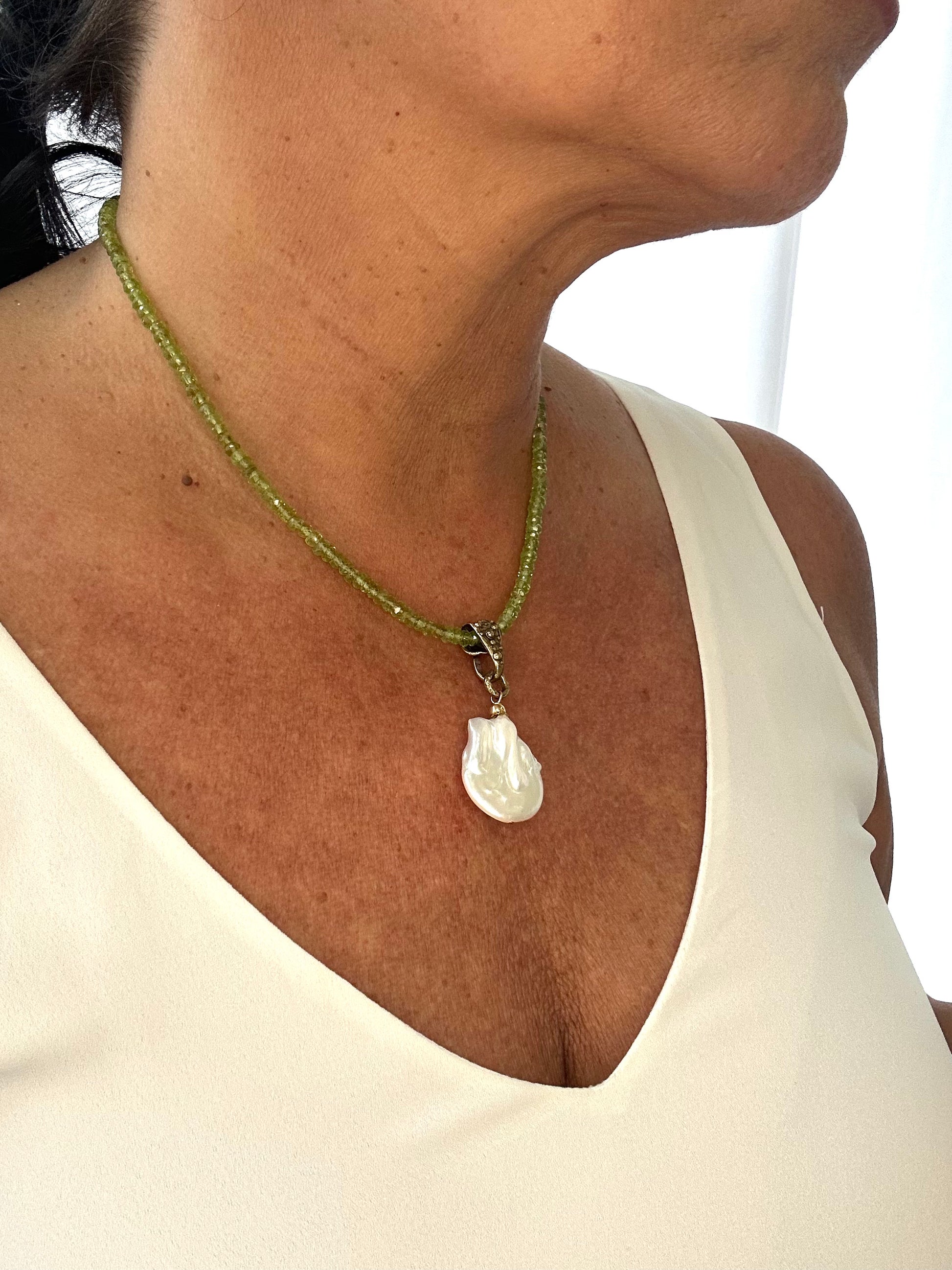 Close-up of a necklace with a shell pendant on a person wearing a white top.