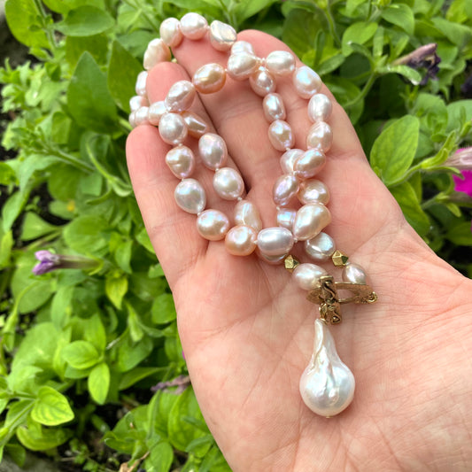 Pink pearl necklace with baroque pendant held in hand against green foliage